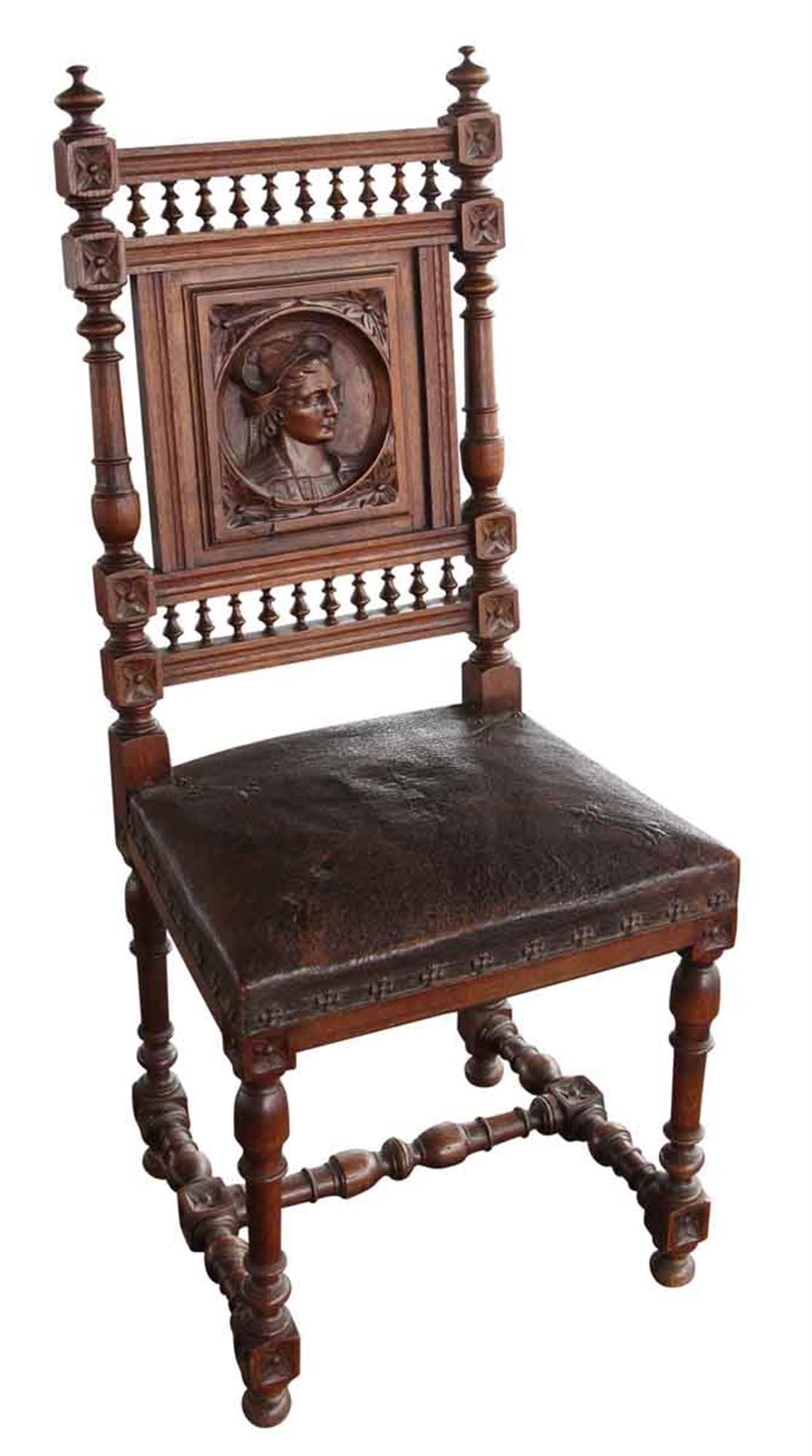 Dark wood tone 1880s English Renaissance style carved chairs with brown leather seats. Each chair back has a different carved face, and every seat cover has the same decorations. The chairs are in excellent condition, but one seat has a rip in the