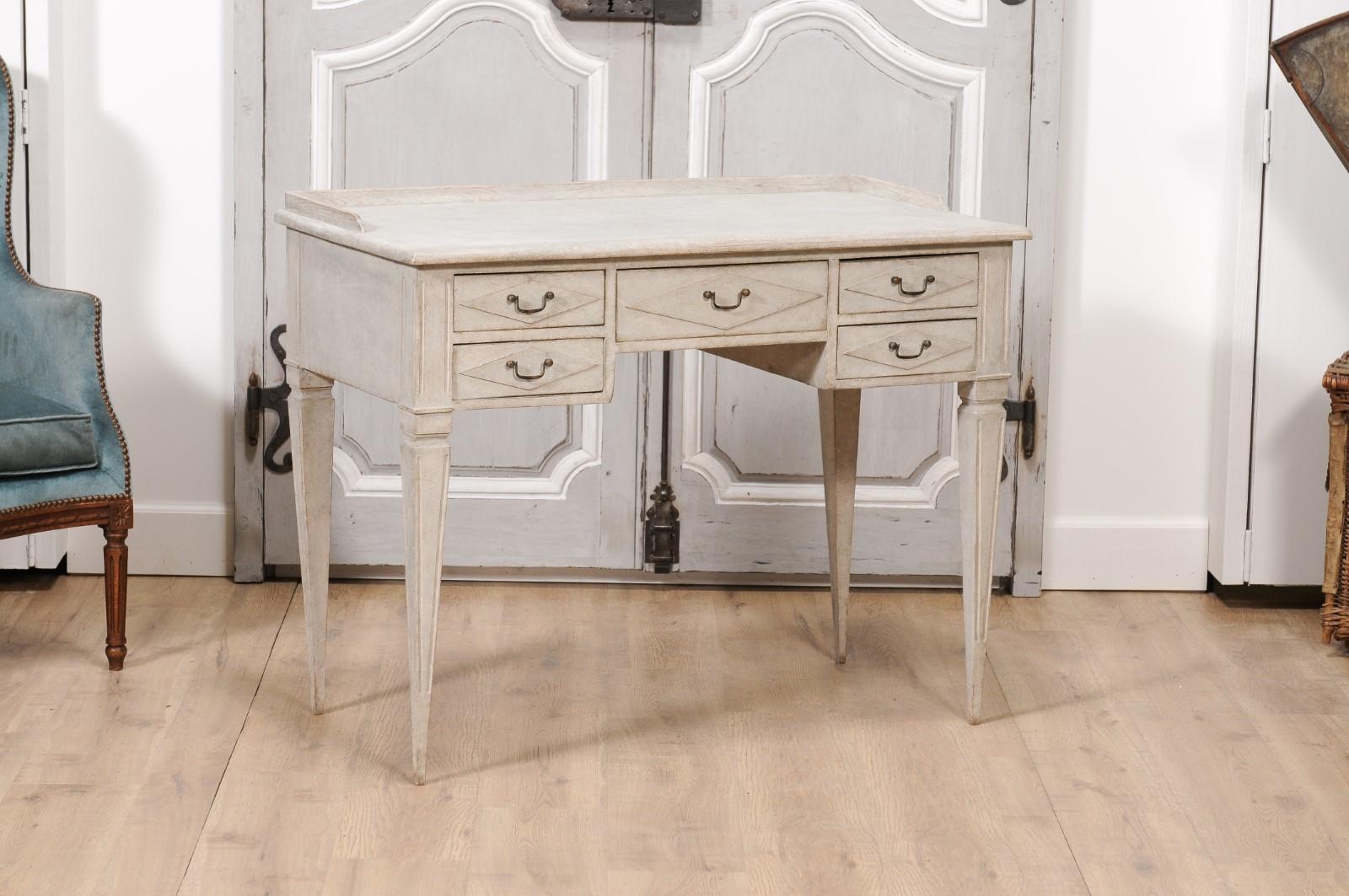 A Swedish Gustavian style painted wood writing table from circa 1880 with five drawers, carved diamond motifs, fluted tapering legs and slightly raised back. Exuding an elegant simplicity typical of Scandinavian design, this Swedish Gustavian style