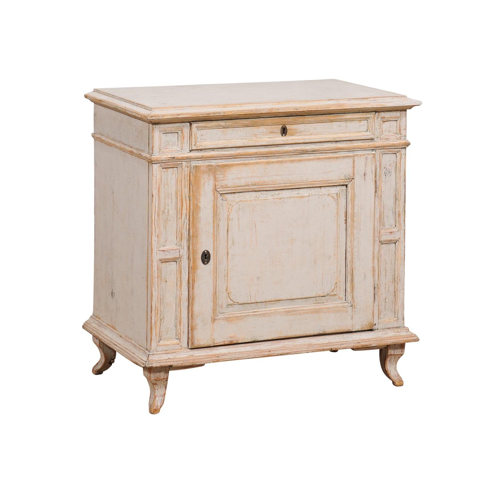 A Swedish neutral light/medium grey painted wood cabinet from circa 1880 with single drawer over single door, wood showing through, recessed panels with molded accents and petite curving feet. Grace your home with the timeless sophistication of this
