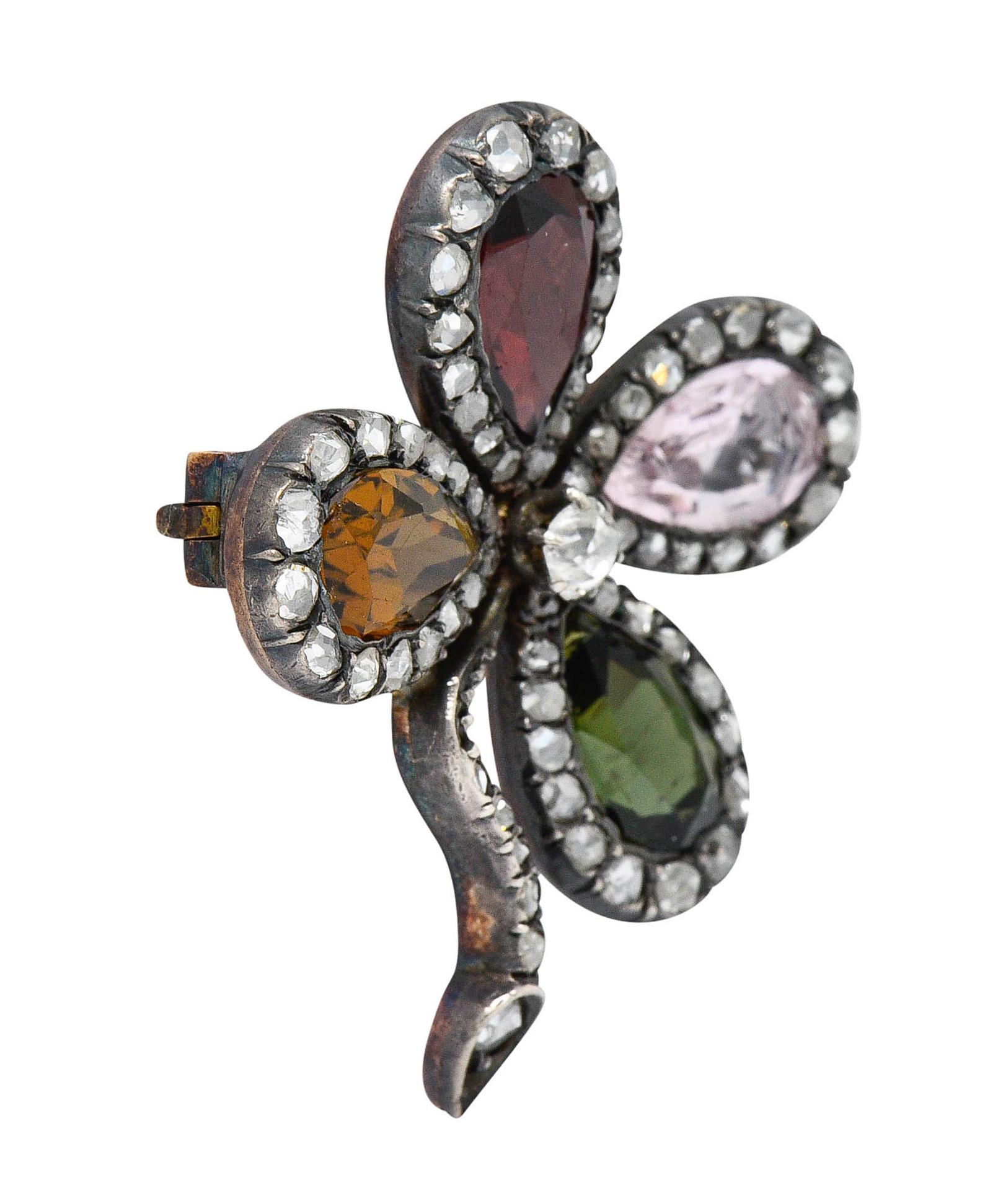 Brooch is designed as a stylized four leaf clover with each petal as a pear cut gemstone

Garnet, Tourmaline, and others - measuring approximately 9.3 x 5.5 mm

Centering an old mine cut diamond weighing approximately 0.15 carat - J/K color with SI