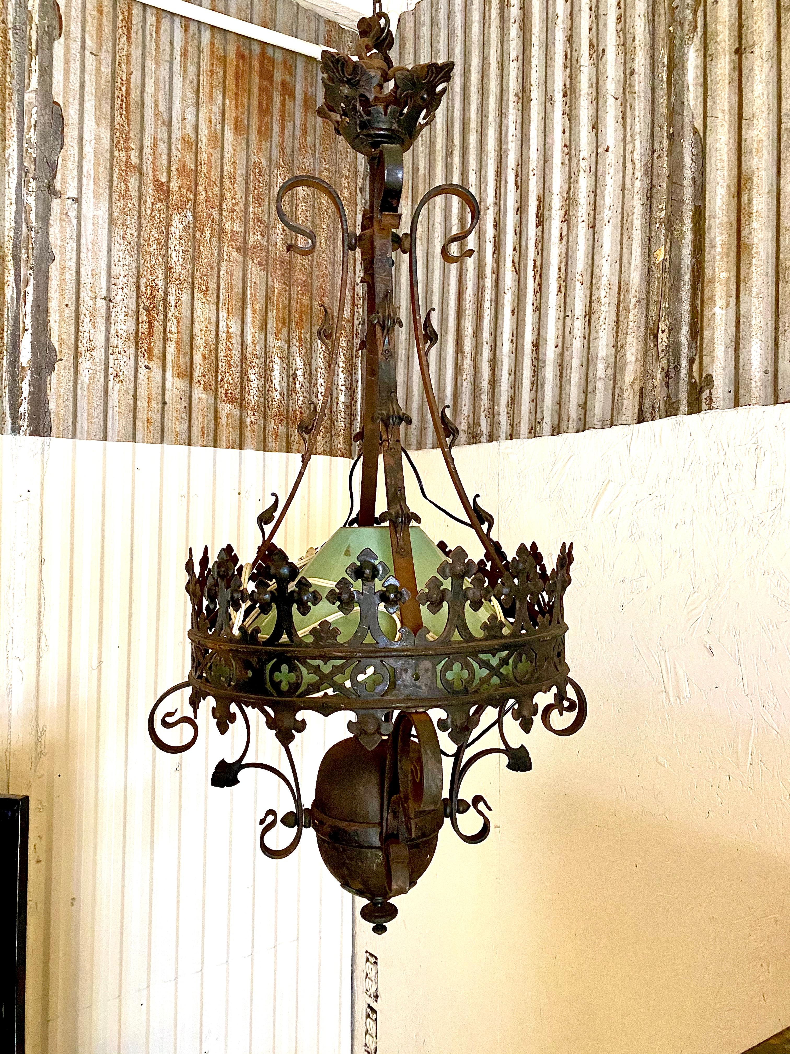 This wrought iron American Gothic light was originally an oil lamp from the 1880s. The light was turned into an electrical chandelier around the 1920s. This light is exquisite and has the original milk glass shade and a profusion of handwrought