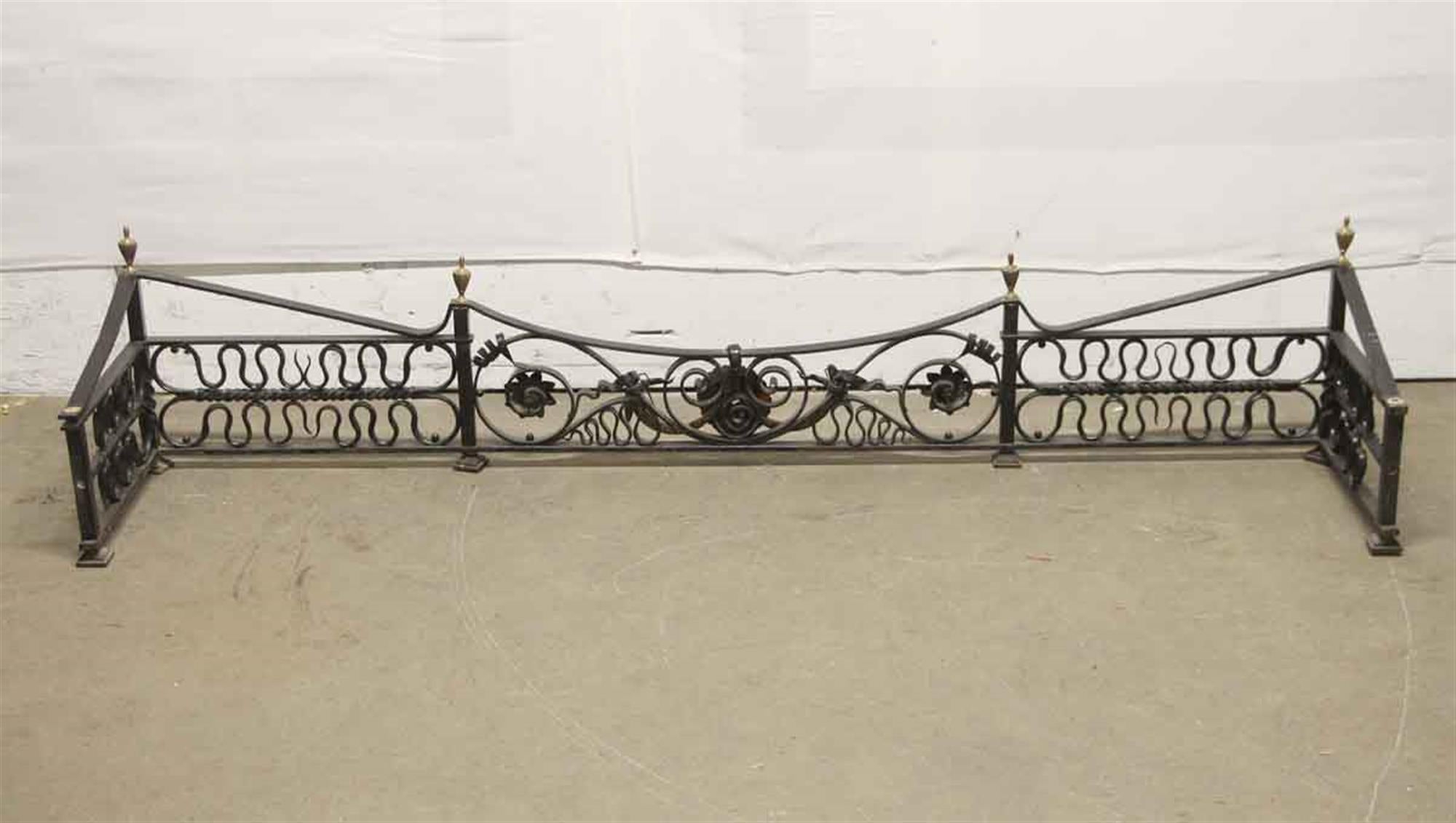 19th century wrought iron fireplace fender with intricate black finished ironwork and brass finials. There is general wear from age and use. This can be seen at our 400 Gilligan St location in Scranton, PA.