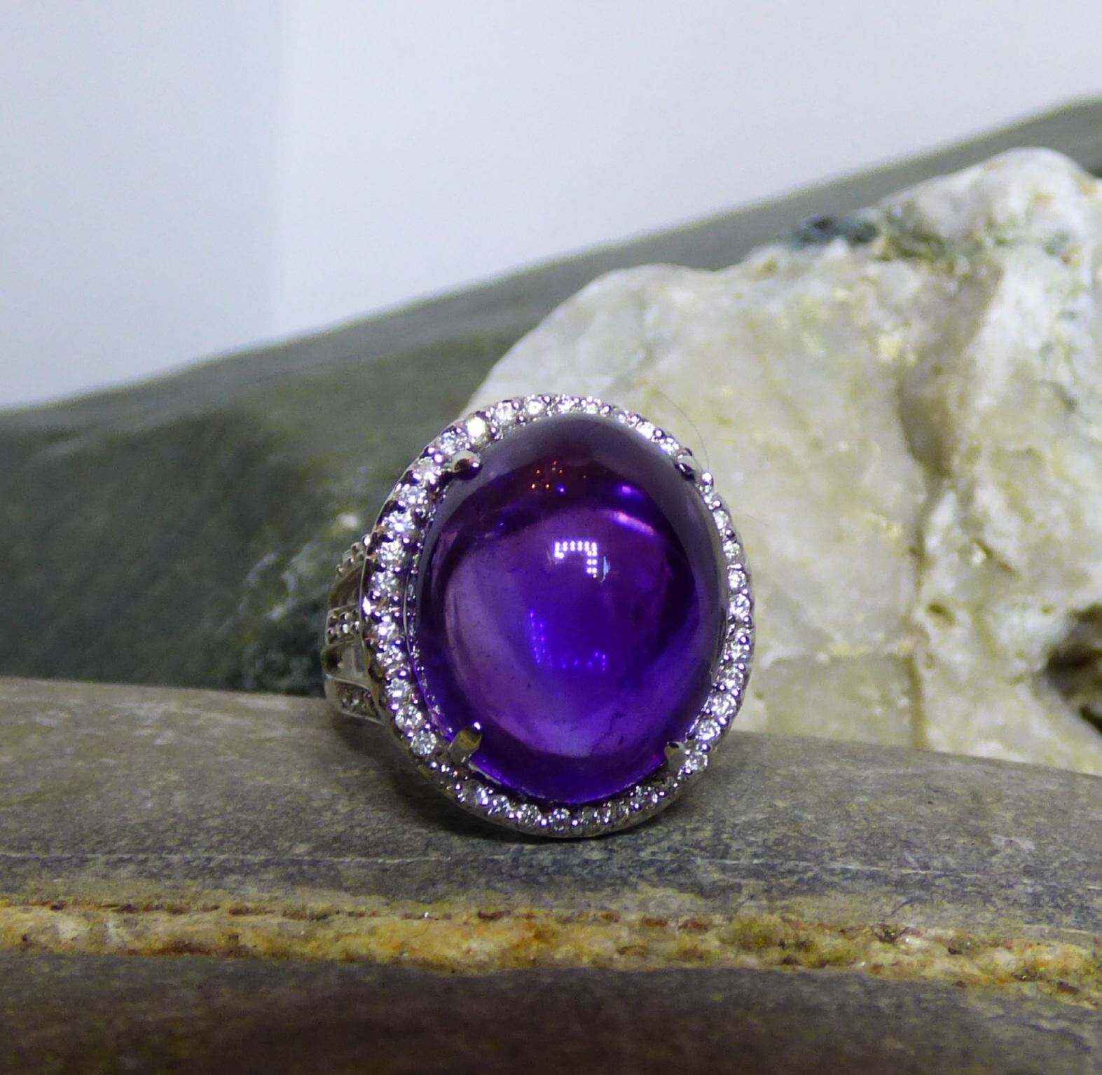 Without facets, this Amethyst stands out with brightness and colour.  The 18.80ct. Cabochon Amethyst is surrounded by Diamonds and the triple split shank is also set with Diamonds. There is a total of 76 Diamonds with a total Diamond weight of