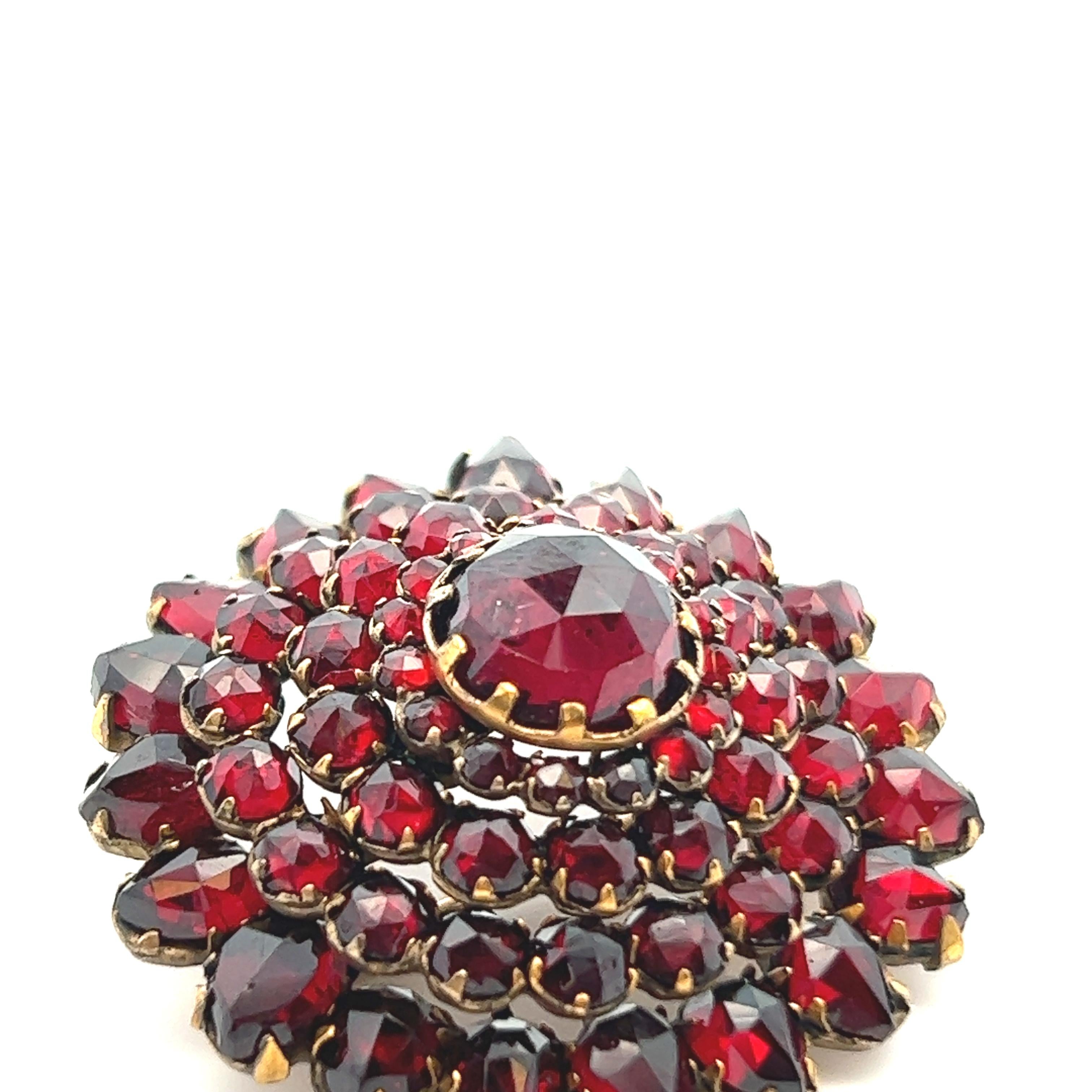 This beautiful 1890 Victorian circle pin is gold gilt over sterling silver with tiered garnet. The pin features a large 8.50mm garnet center stone, surrounded by four more layers of varying sized garnet (2.00mm-8.50mm) to give the pin a full garnet