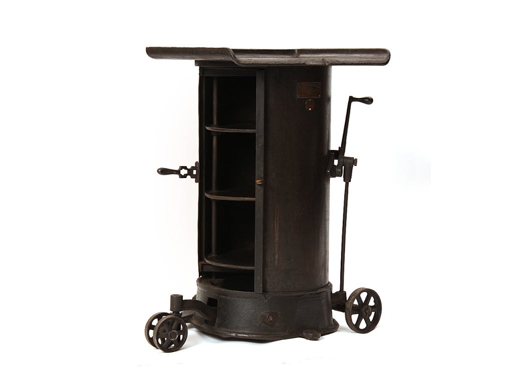 An Industrial cast iron rolling cabinet on three wheels with three concealed interior storage shelves. Retaining the original brass makers mark.
