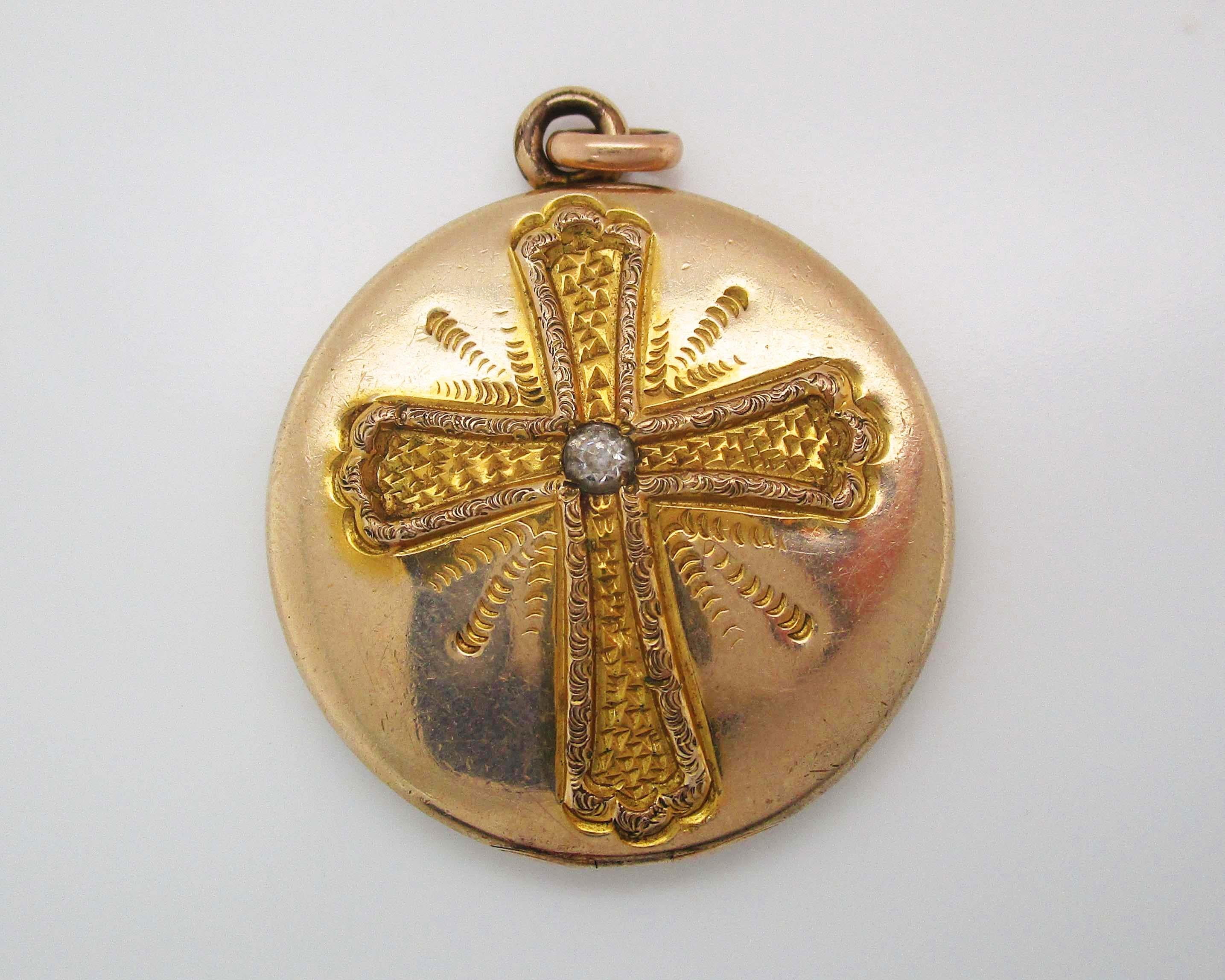 From the treasure troves of the past comes this stunning round two photo gold locket hand engraved with an elegant cross design and set with a beautiful white stone center. The front of the locket bears a lovely textured cross design while the back