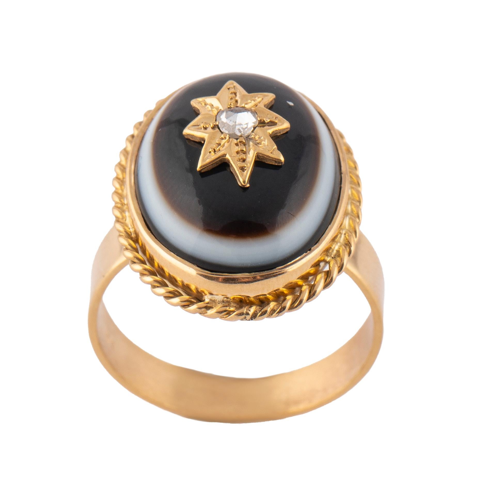 Dieser Ring aus 14-karätigem Gelbgold ist mit einem ovalen spätviktorianischen Stieraugen-Achat besetzt, der von einem Diamanten im Rosenschliff auf einem goldenen Sternmotiv in einer gedrehten Tauwerk-Bordüre zentriert wird.

Ovale Lünette: 2,2 cm