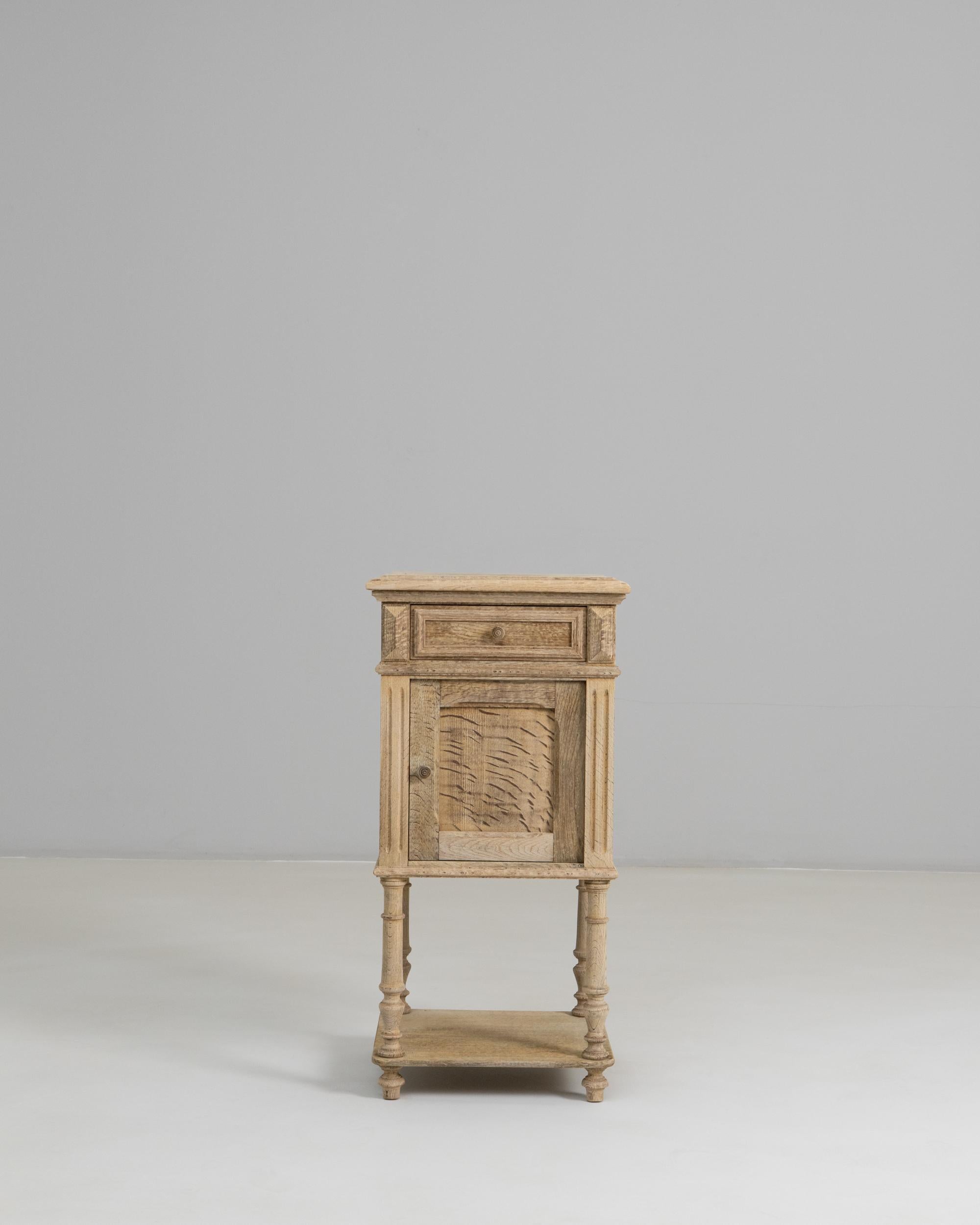 This 1890s French oak bedside table combines delicate carved detailing with the rustic charm of provincial craftsmanship. Its upper drawer and paneled door are framed by fluted side supports, adding subtle architectural interest while showcasing the