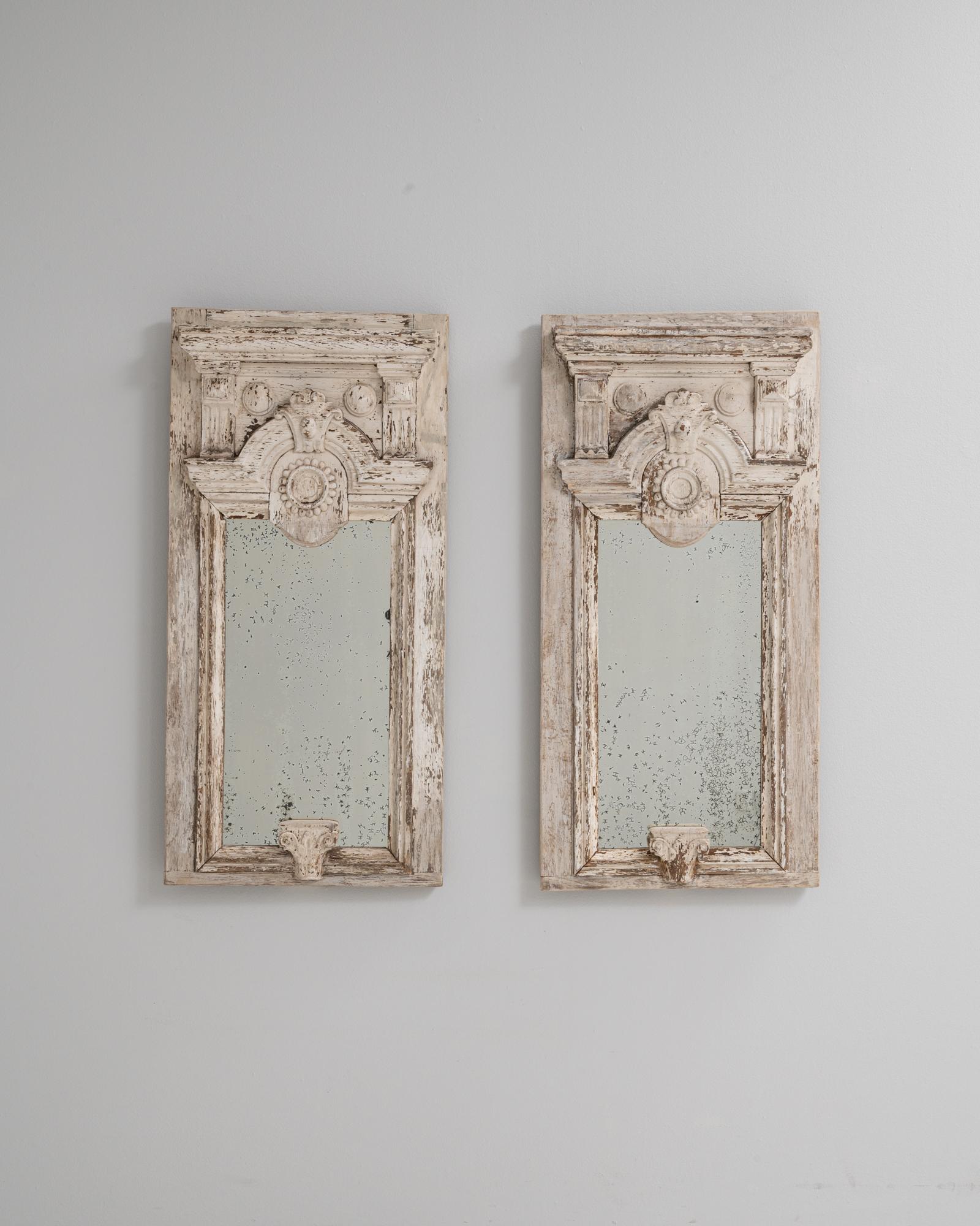 Cette paire de miroirs français des années 1890 présente des cadres en bois ornés d'une patine blanche très usée, révélant les traces du bois naturel. Des éléments architecturaux richement sculptés - notamment des volutes, des rondeaux et un motif