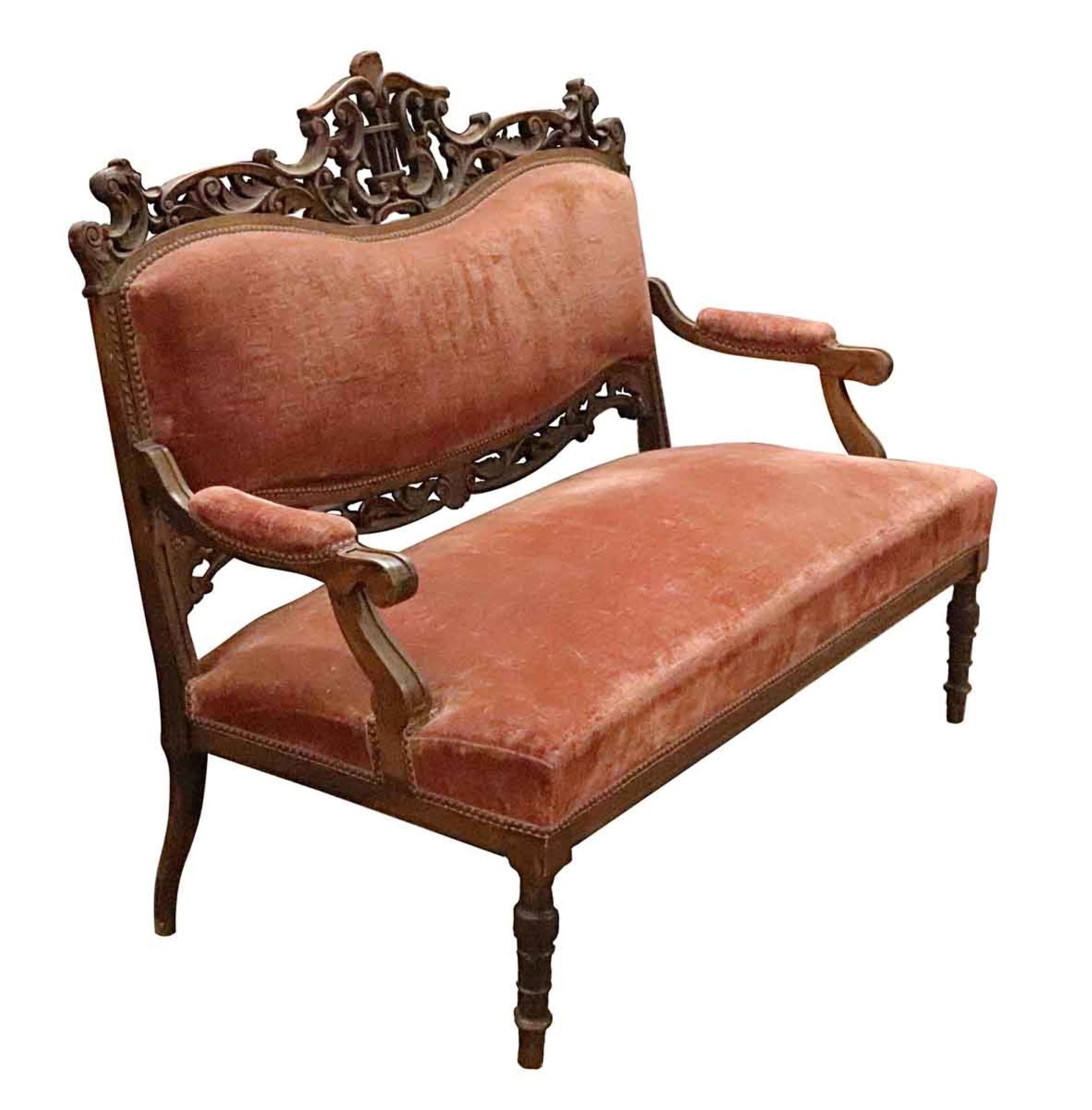 1890s Victorian red velvet love seat from France. The frame is heavily carved and made of walnut or oak with a musical motif.