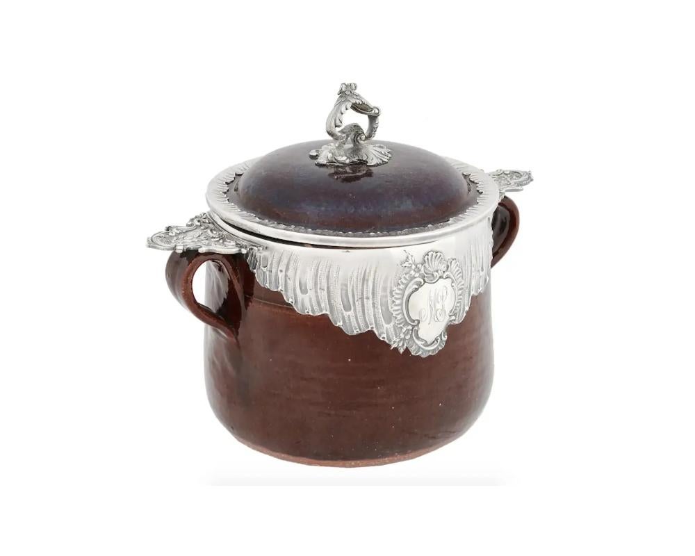 An antique late 19th century French glazed earthenware two-handled lidded pot with sterling silver mounts and lid handle. The richly decorated mount has an engraved monogram MP on the front side. Hallmark HC is on the rim. Embossed letter J is on