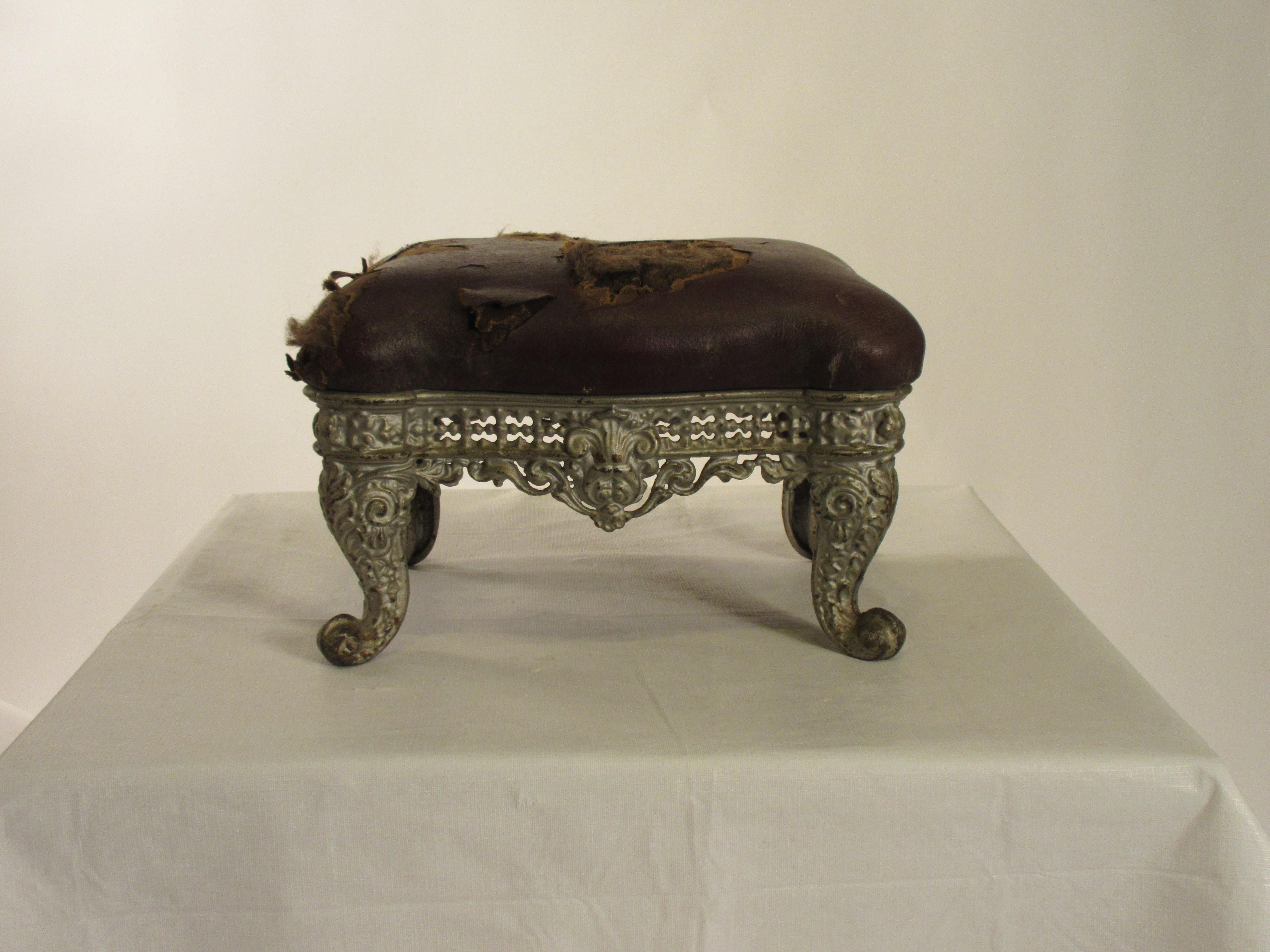 1890s iron ornate footstool with original leather. Needs reupholstering.