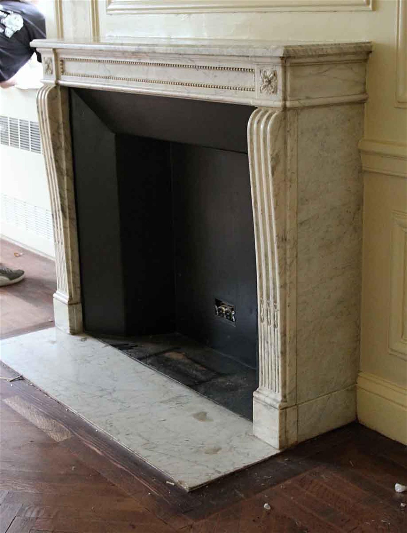 1890s French Regency Louis XVI style white hand carved marble mantel with gray veining and decorative detail along the header and floral motifs on the top plinths. This mantel was one of a group of antique mantels imported from Europe and installed