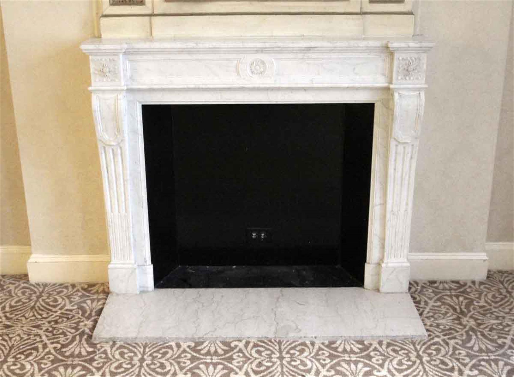 French Regency style white Carrara gray veined marble mantel with carved legs and floral motifs in the middle of the header and top plinths. This mantel was one of a group of antique mantels imported from France and installed in the NYC Waldorf