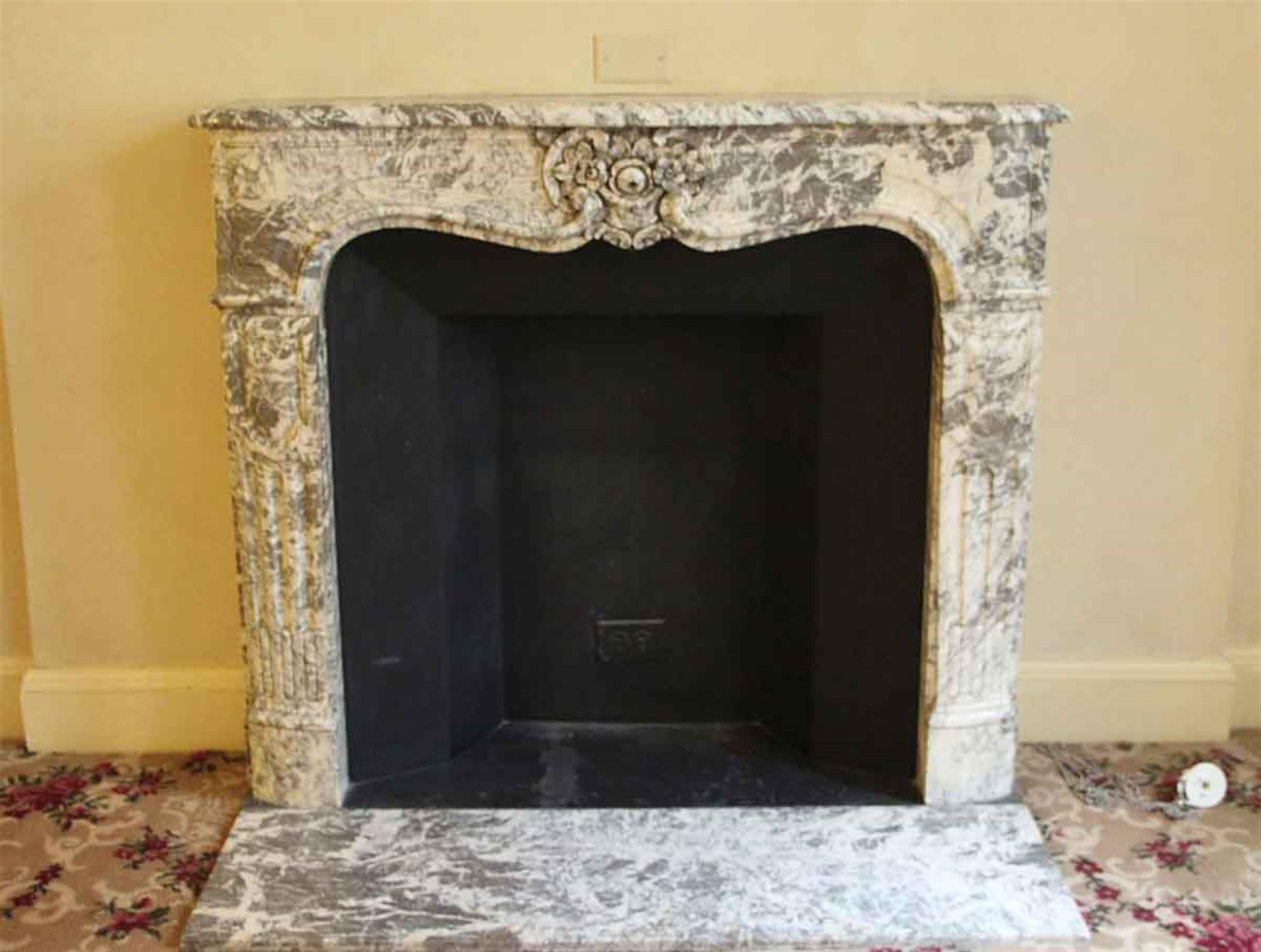 French Louis XV Rococo style gray and white marble mantel with the original matching hearth. This mantel was one of a group of antique mantels imported from Europe and installed in the Waldorf Astoria hotel in the 1930s when the hotel was first