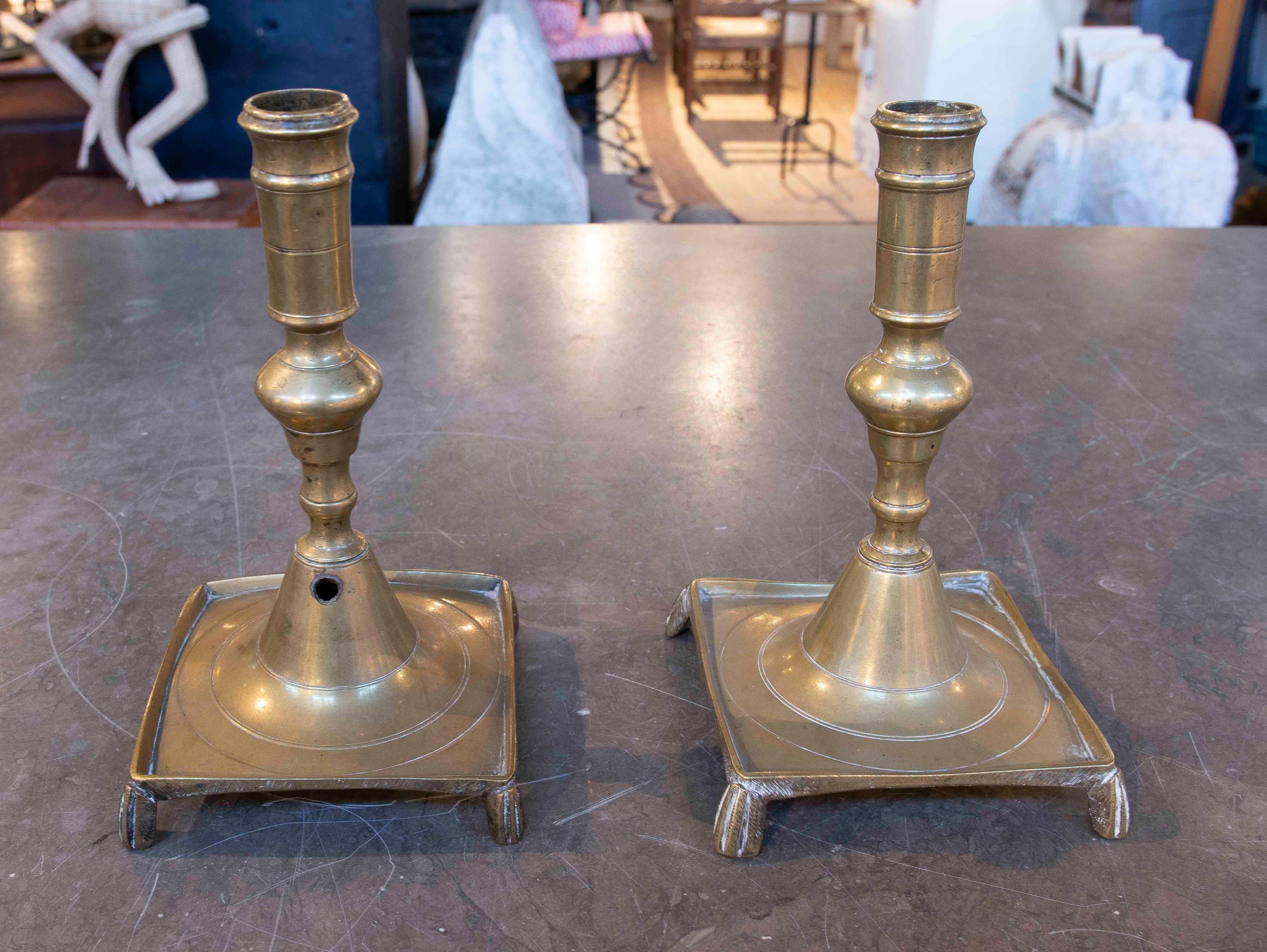 Elegante coppia di candelieri spagnoli realizzati in bronzo, con un design classico che combina una struttura tornita con una base quadrata leggermente rialzata su gambe decorative. La loro finitura lucida e i dettagli lucidi aggiungono un tocco di