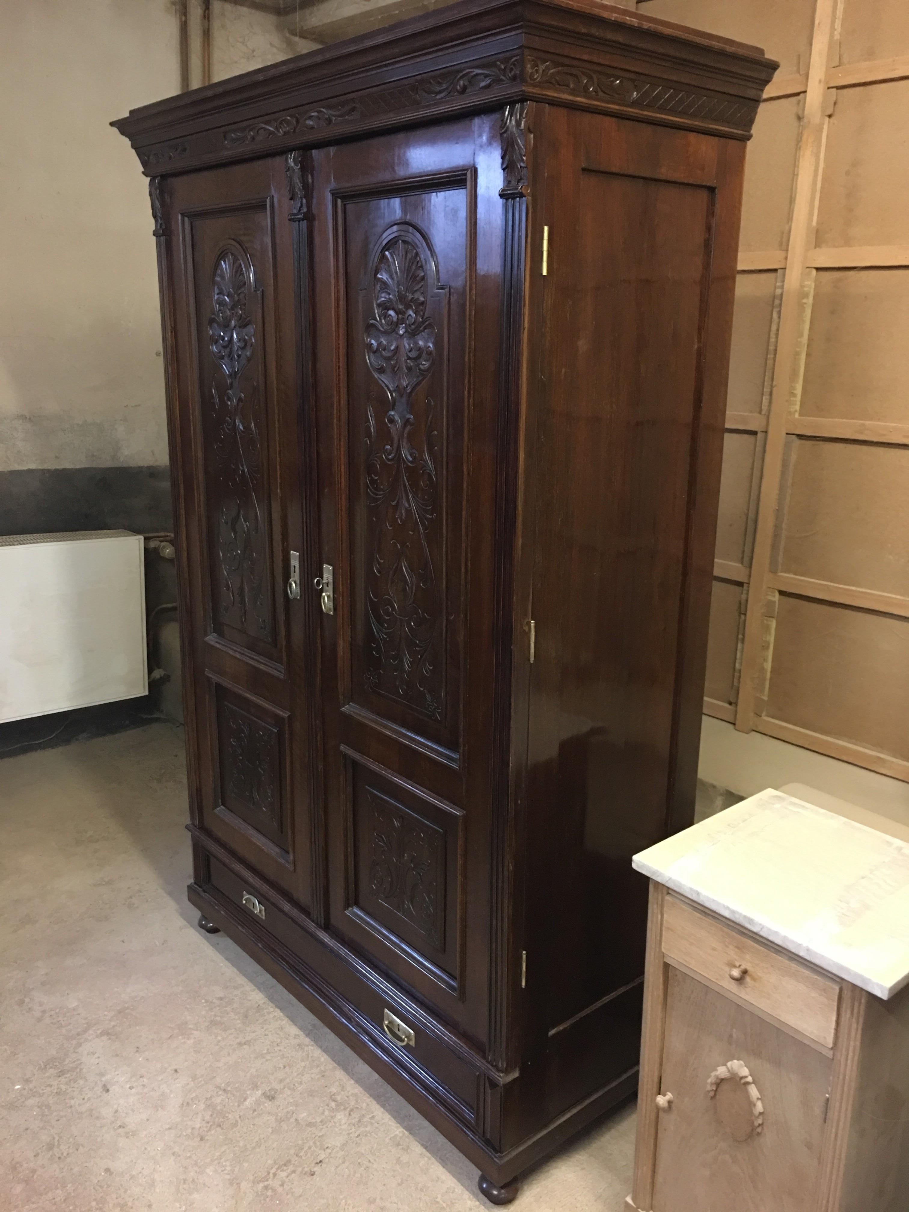 This is a Gründerzeit walnut wardrobe, which was polished up with shellac by hand. Finest volutes carvings on the doors decorate the elegant piece. The dark brown walnut wood gives the piece a rustic charm, which is reinforced by brass fittings.