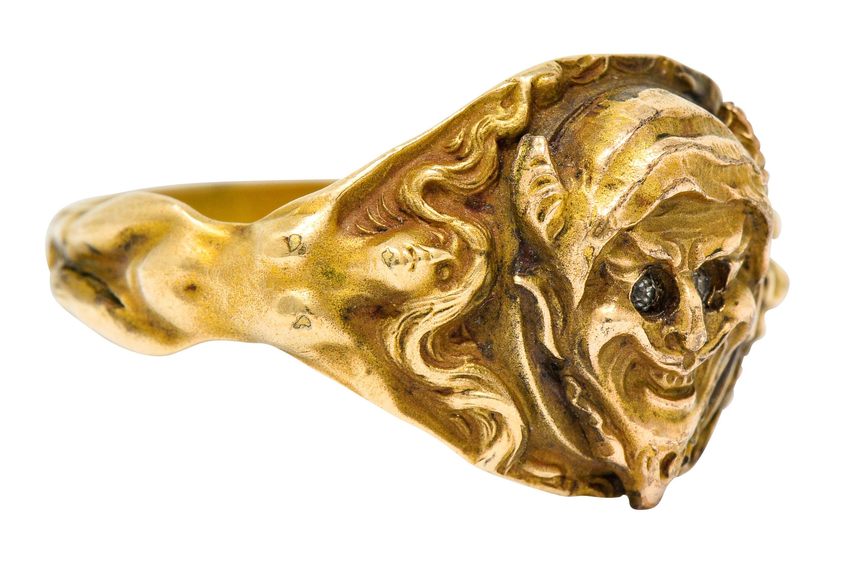 Band style ring depicting a grimacing devilish face, hooded and with horns, incredibly detailed

Eyes are accented by paste gemstones, glittering and white

Shoulders are comprised of two female figures with open arms and windswept hair

With