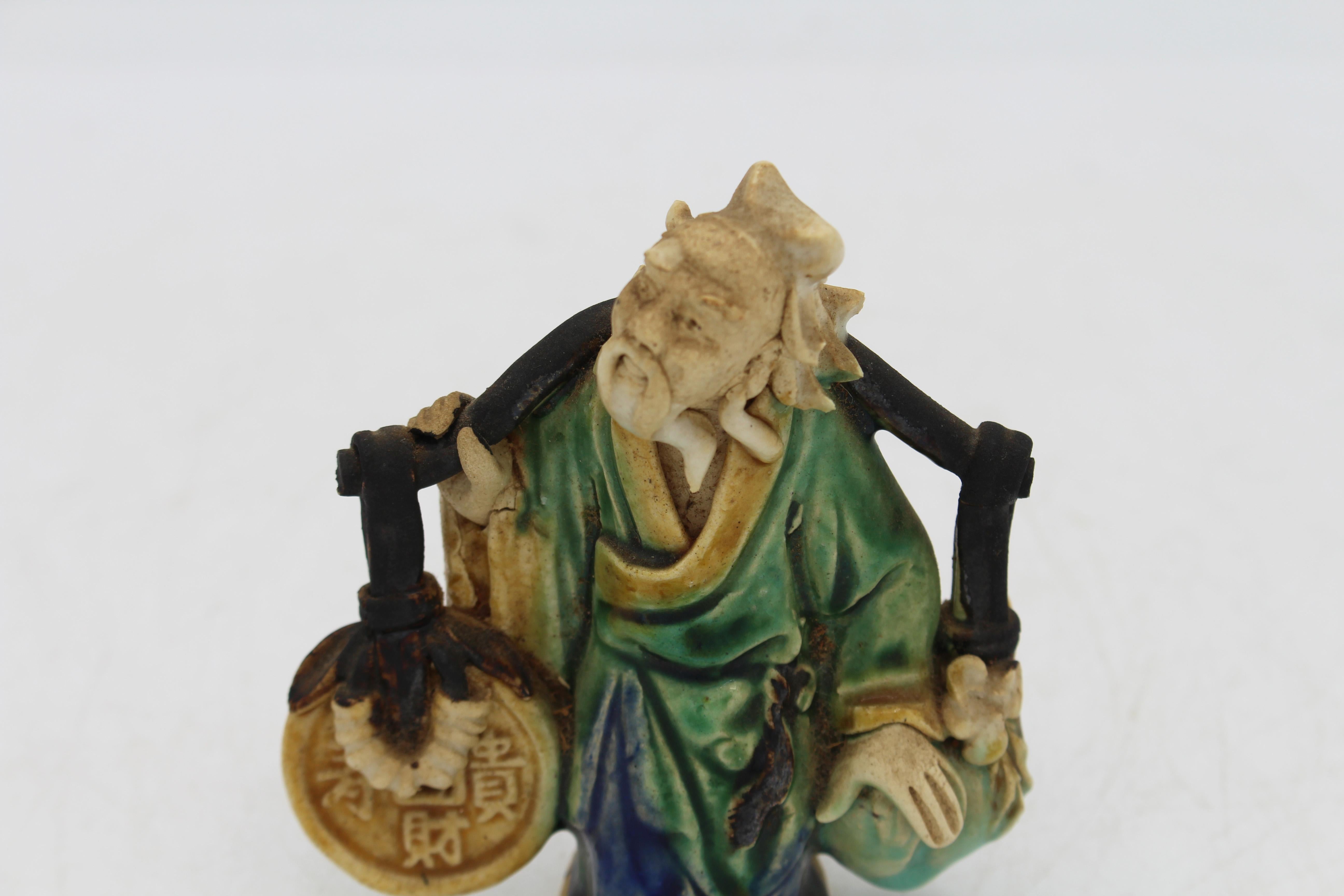 Souvenir dell'Esposizione Universale Cinese del 1891-1911: figura dell'uomo di fango. Viso meravigliosamente espressivo; vestito con una tunica verde con rifiniture gialle. Porta con sé un giogo a tracolla con una pesca gigante su un lato e
