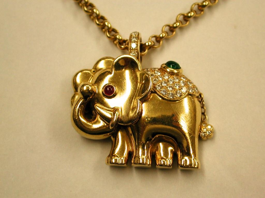 18ct Gold Elephant Pendant  On Chain set with Diamonds,Emerald & Ruby, 1995.
This elephant pendant and chain is made out of a heavy quality gauge of gold.
It has a cabochon ruby eye and studded brilliant cut diamonds on the top with a cabochon