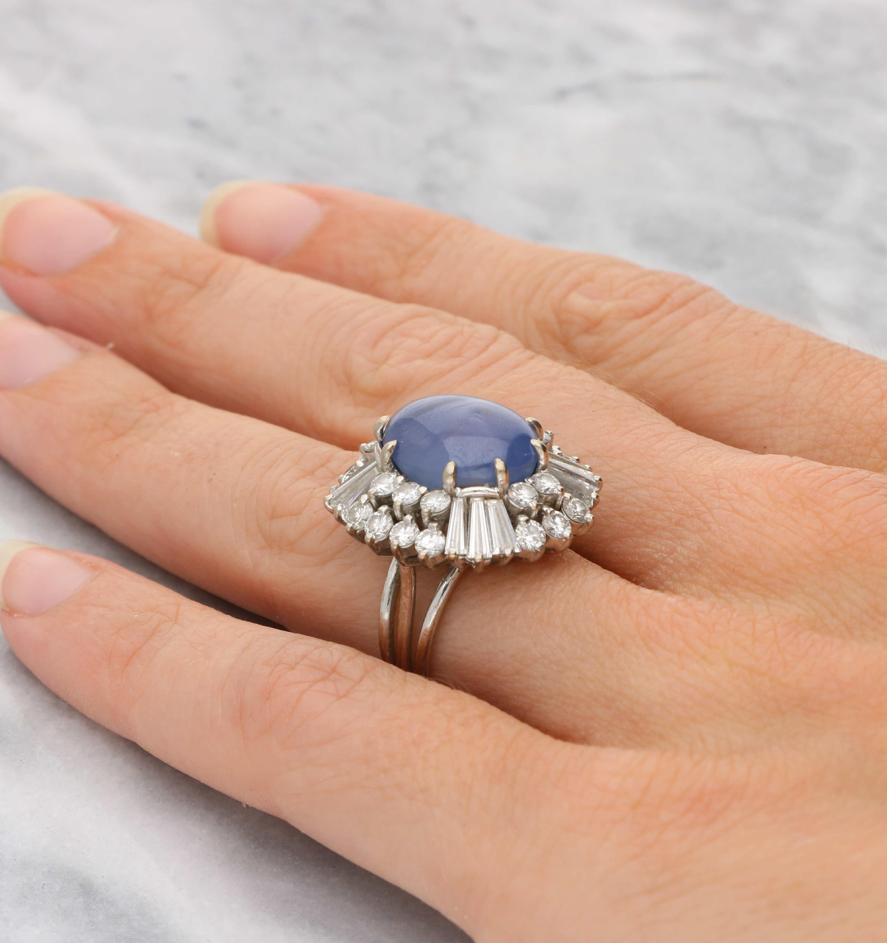An 18ct white gold star sapphire and diamond cluster ring. The sapphire has an estimated weight of 12.00ct and is surrounded by 2.50ct of tapered baguette & round brilliant diamonds. The head of the ring measures 23x21mm and is a UK size L / US size