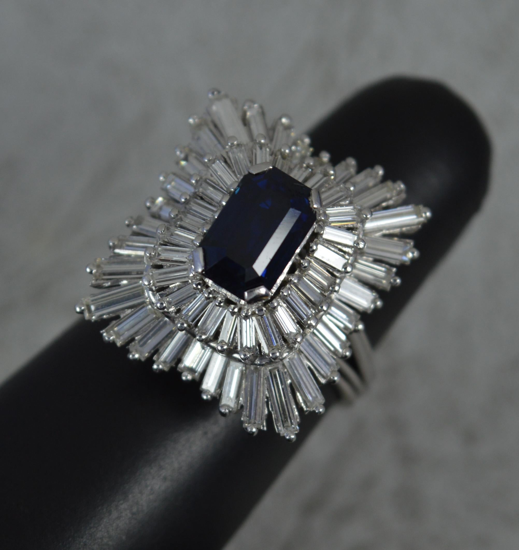 A highly unsual and striking ballerina cluster cocktail ring.
Solid 18 carat white gold example.
A three tiered cluster. Designed with an emerald cut blue sapphire to the centre, 5.5mm x 8.7mm. Surrounding are many baguette cut diamonds of varying