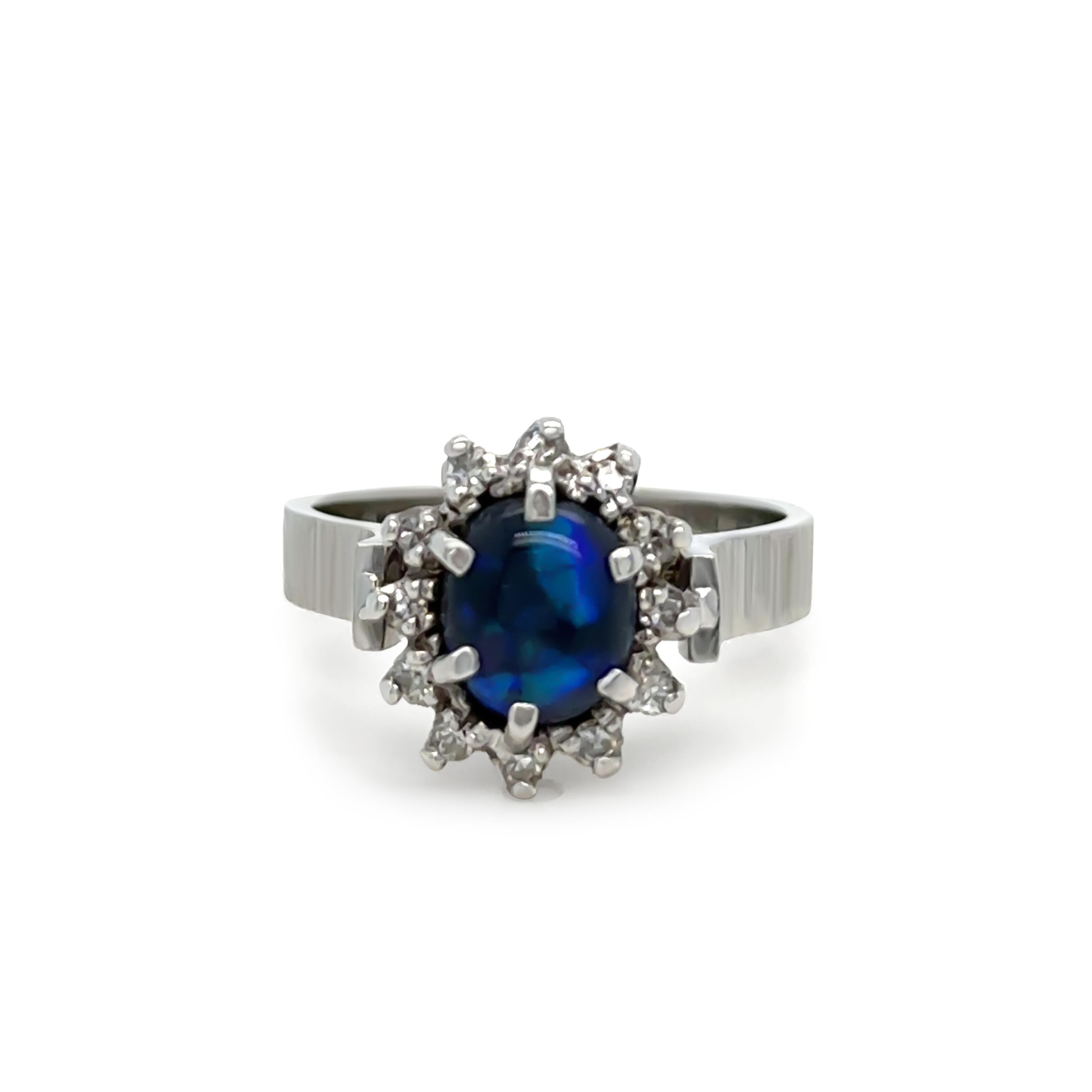 This exquisite black opal and diamond cluster ring is crafted in 18ct white gold, featuring a striking 0.62ct Lightning Ridge black opal. The opal measures 7.2 x 6.2mm and showcases a mesmerising green and blue flash, making it a standout