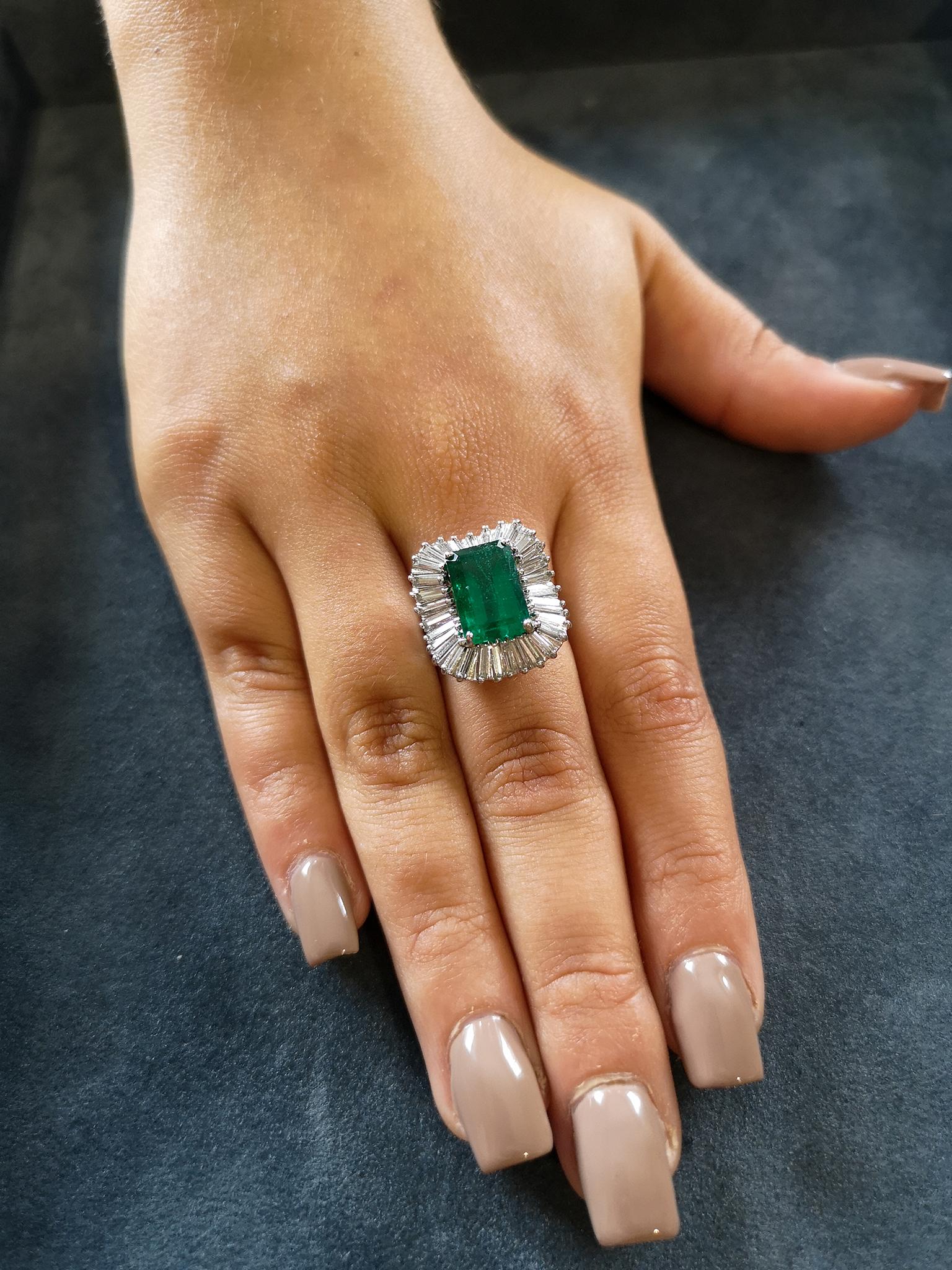  A deep, grassy green emerald-cut emerald of approximately 4.00 carats, mounted in four claws is surrounded by a undulating 'tutu' of tapered baguette-cut diamonds, approximately 1.50 carats in total, H colour, SI clarity. The reeded shank