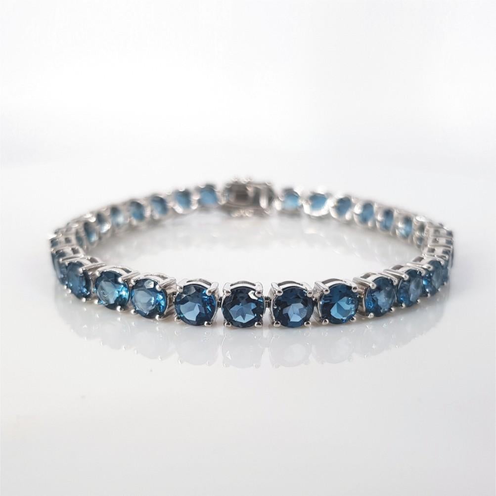 Dieses wunderschöne, mit Nieten besetzte Tennisarmband ist in 18 Karat Weißgold gefasst, wiegt 15 Gramm und misst 18,7 cm in der Länge, 4 mm in der Breite und 3,5 mm in der Höhe. Dieses Armband enthält 31 Londoner Blautopase mit einem geschätzten