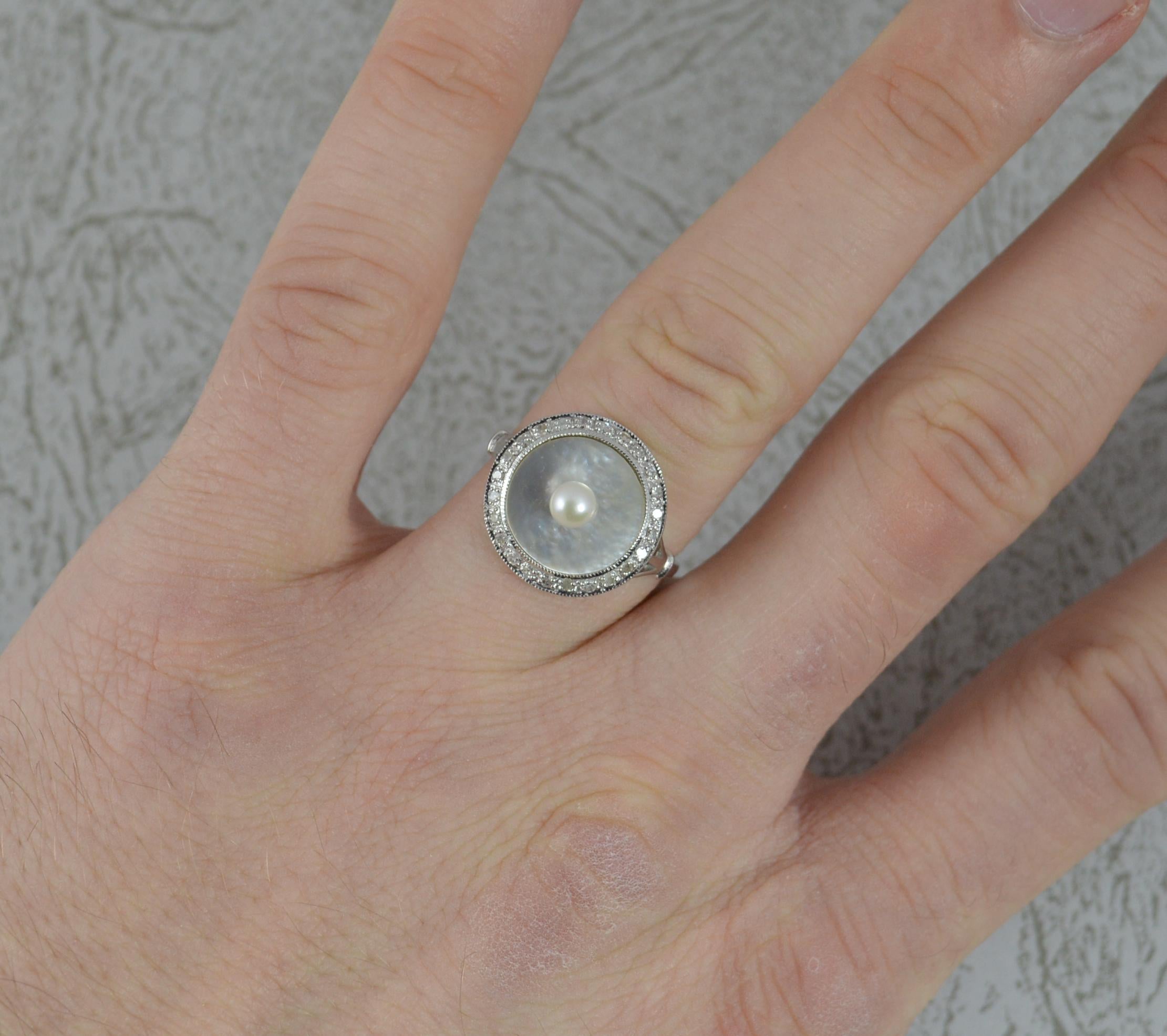 A superb 18ct gold, mother of pearl, pearl and diamond panel ring.
18 carat white gold example.
15mm diameter circular panel head.
Formed with a pearl to the centre applied onto a mother of pearl panel. Surrounding are over 25 natural round cut