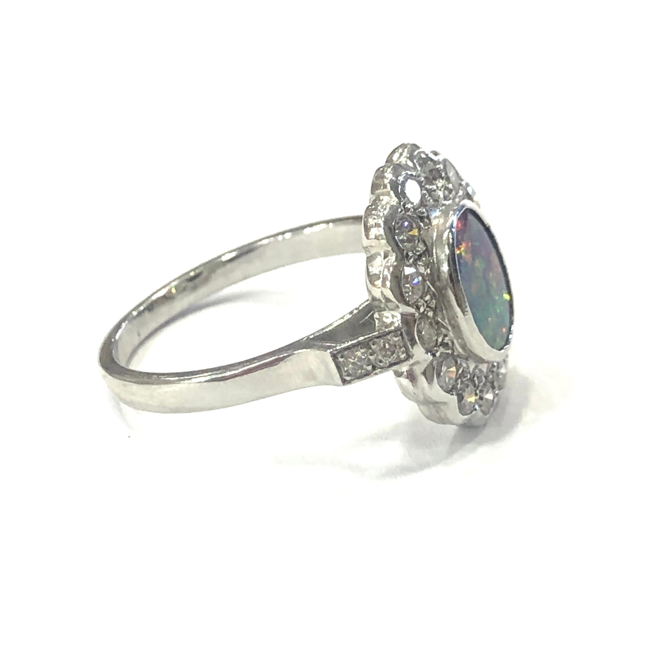 18ct White Gold Opal and Diamond Cluster Ring. Set with one central oval Australian Opal in a rubber setting, surrounded by fourteen round brilliant cut diamonds and two diamonds on each shoulder.

Approximate Opal weight : 1.20ct
Approximate total