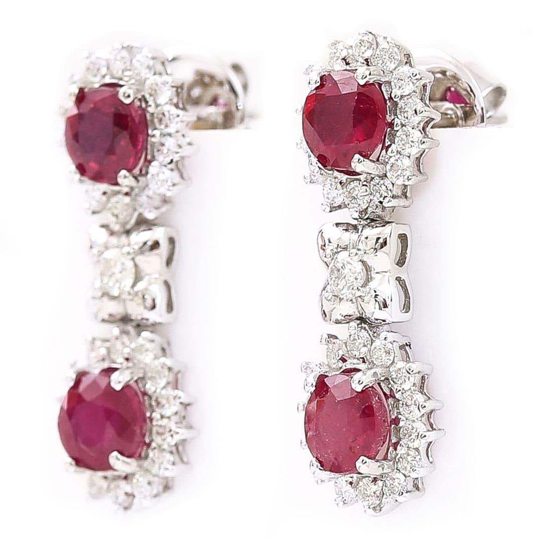A beautiful pair of contemporary polished 18ct white gold oval cut ruby and brilliant diamond drop earrings. The earrings are formed of two oval clusters centrally set with a deep red, oval cut ruby surrounded by a cluster of claw set brilliant cut