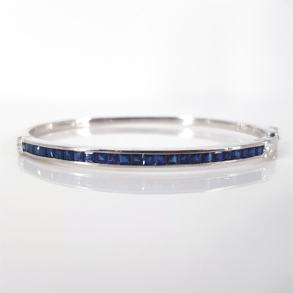 This elegant bangle is set in 18 carat White Gold featuring 25 Princess Cut Sapphire Stones with a total carat weight of 3.75 and 2 round brilliant cut diamonds totalling 0.02 carat of IJ/vs-si quality. Its diameter is 6.5cm and weighs 16.6 grams.