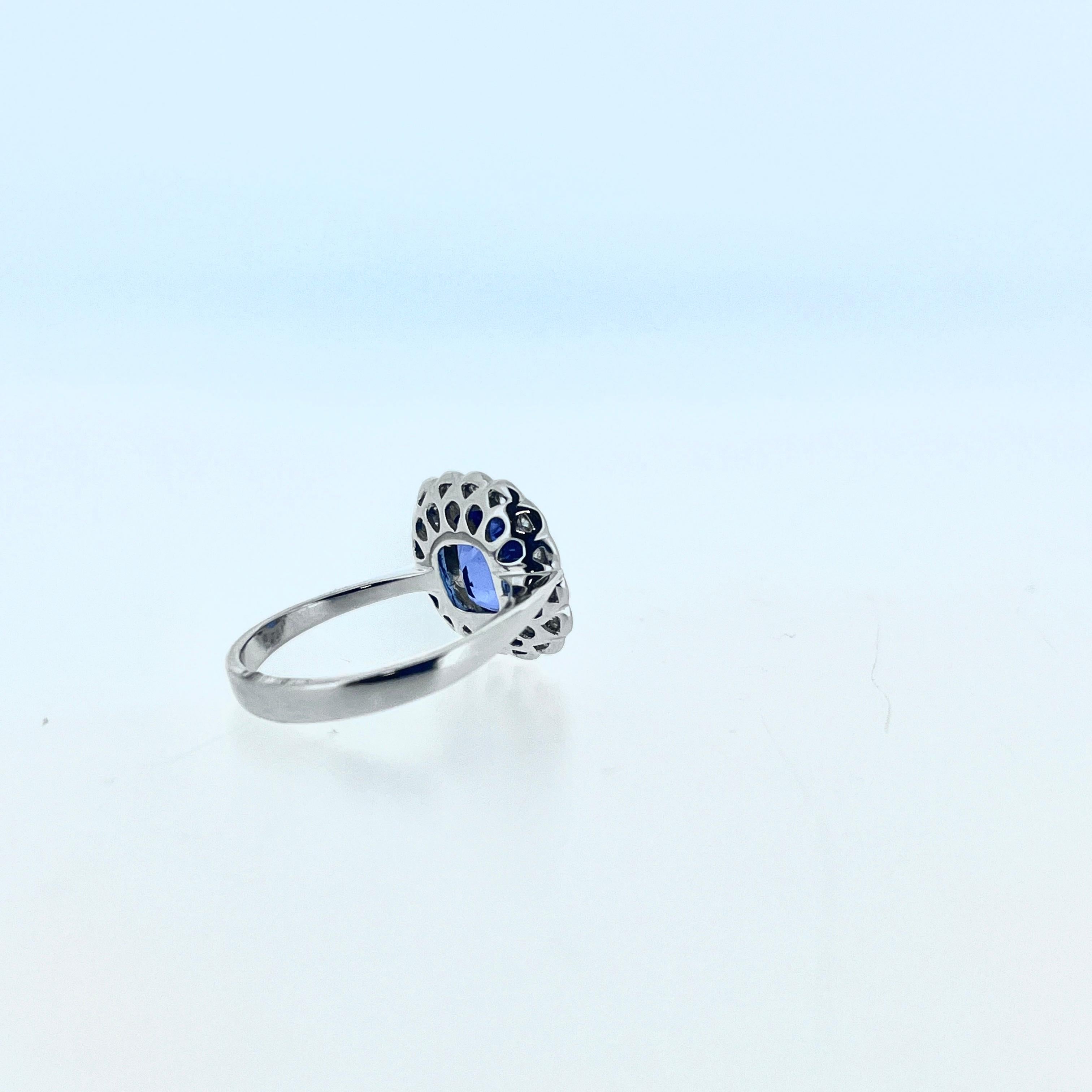 Si vous cherchez une bague en tanzanite et diamant de style ancien, votre recherche est peut-être terminée !  Cette bague en or blanc 18ct est ornée d'une tanzanite de taille coussin, encadrée d'un halo de diamants. C'est le moyen idéal d'ajouter