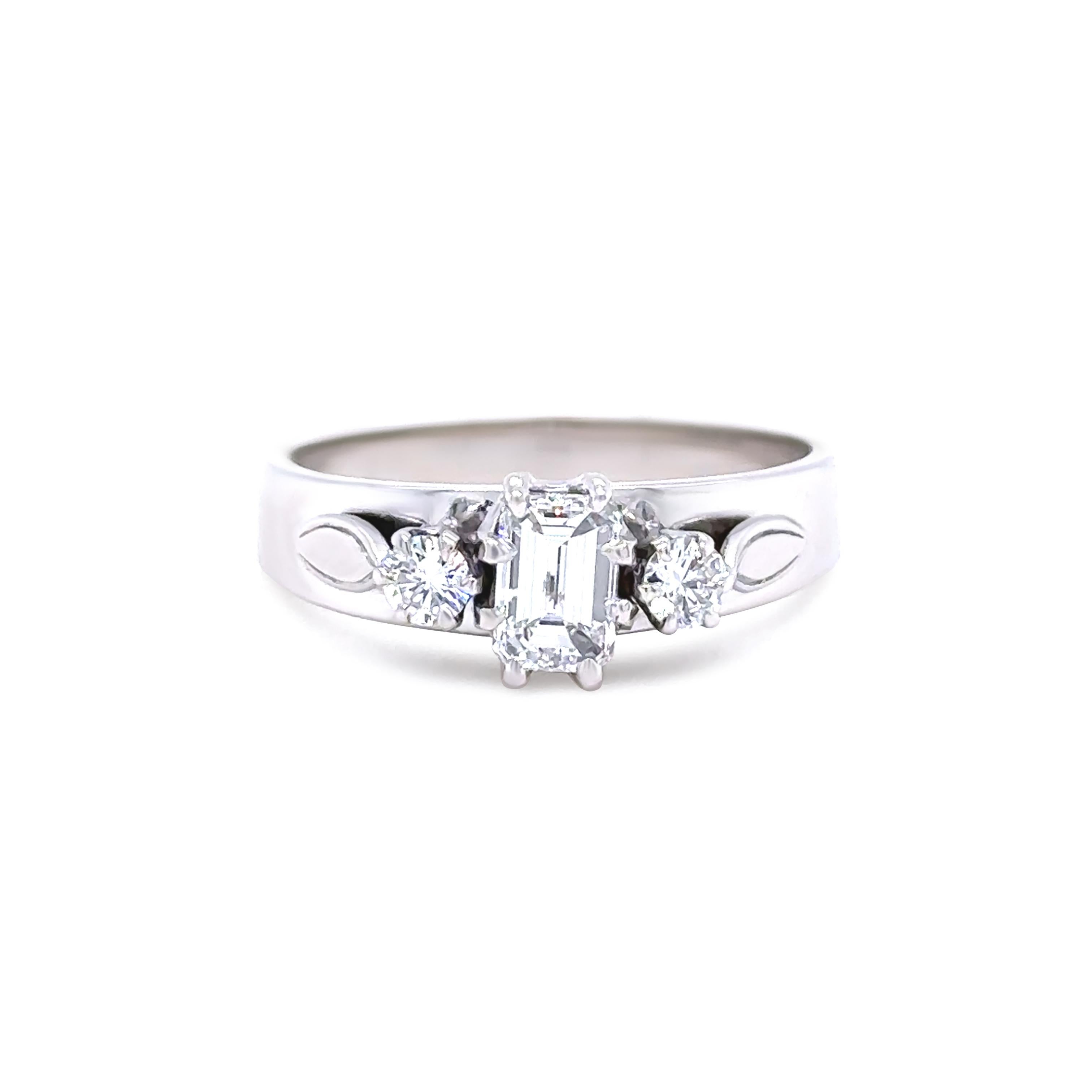 This timeless three-stone ring is crafted in 18ct white gold, featuring a central emerald-cut diamond weighing 0.56ct, graded F colour and VS+ clarity. 

It is flanked by two modern round brilliant-cut diamonds totalling 0.17ct, also graded F colour