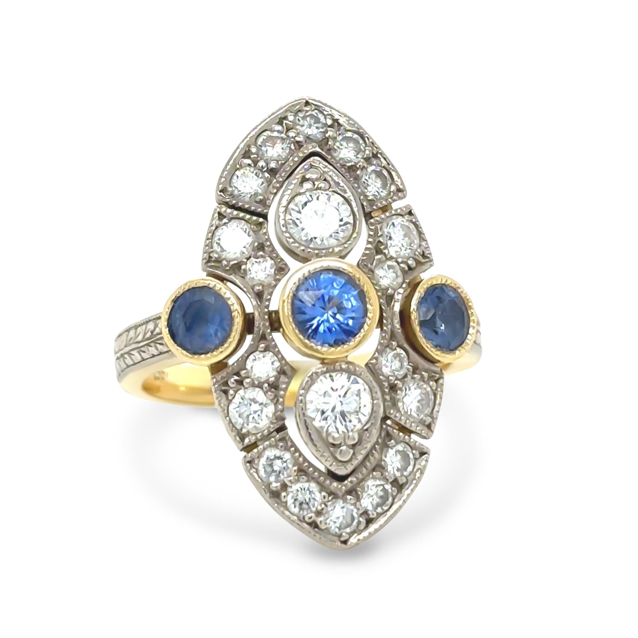 This stunning sapphire and diamond ring is crafted in 18ct yellow and white gold. It features three round-cut blue sapphires in bezel settings, with the centre sapphire measuring approximately 4.60 x 2.92mm and weighing 0.42 carats. The two side