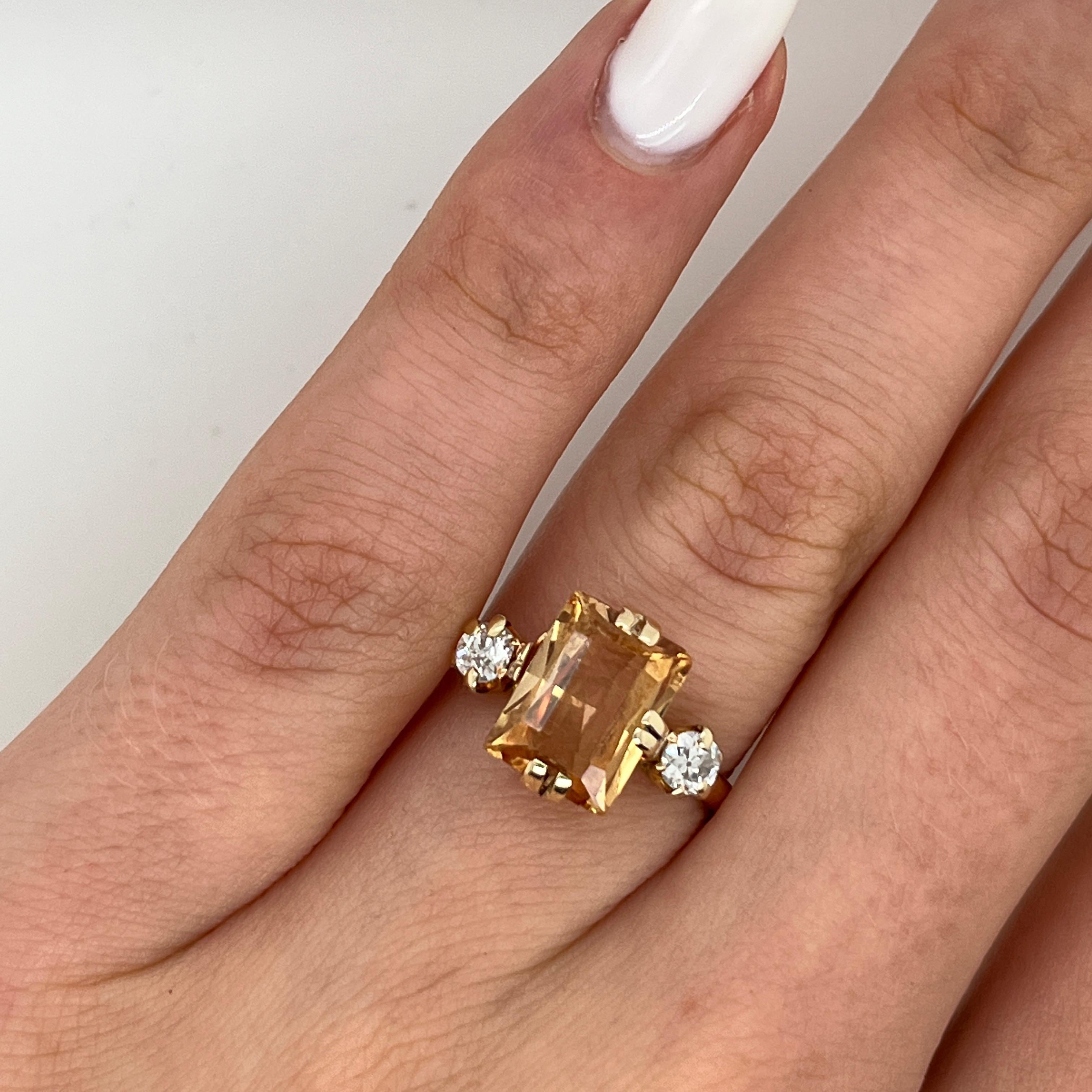 Cette bague classique et élégante en or jaune 18ct est ornée d'une citrine vibrante en son centre. 
Accentuée par deux diamants naturels étincelants, cette pièce allie chaleur et brillance, 
Il s'agit d'une pièce intemporelle qui s'ajoute à toute