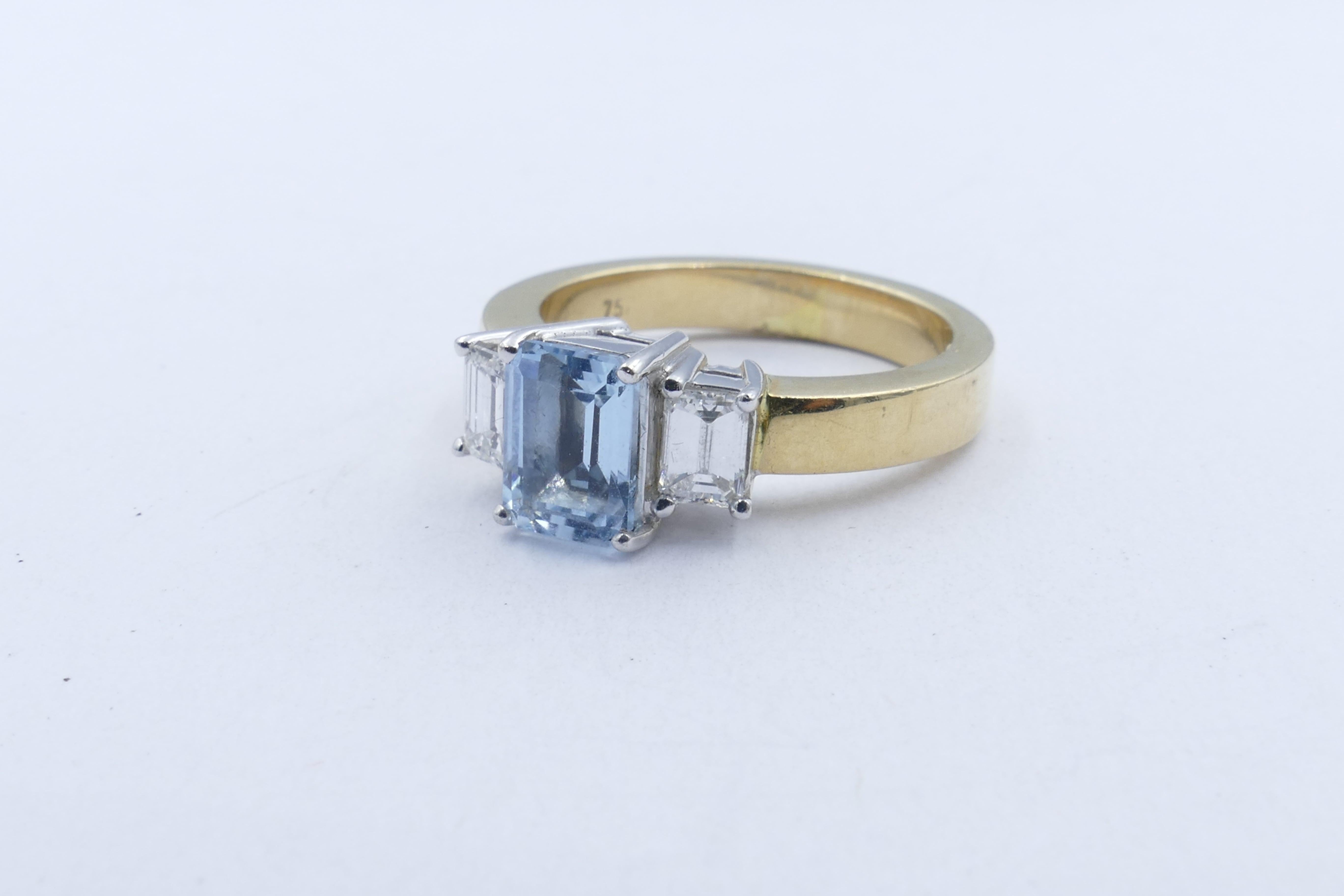 In gorgeous Art Deco Style this very attractive Ring has an Emerald Cut Aquamarine measuring 7.05 X 5.15, 4 claw set, approximately 1 carat, as the centrepiece. The Stone is very pure, eye-clean & vivid blue in colour. 
It is flanked by 2 Emerald