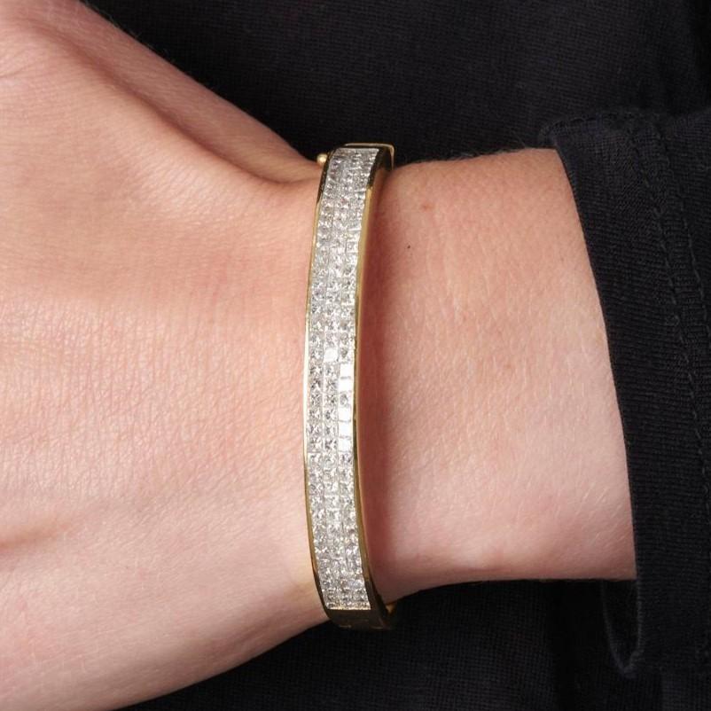 Cet ensemble bangle-boucles d'oreilles assorti présente un design impeccable de diamants taille radieuse en serti-canal, en rangées de trois, parcourant la moitié de chaque pièce. Le bracelet, qui comporte un  Les boucles d'oreilles sont marquées en