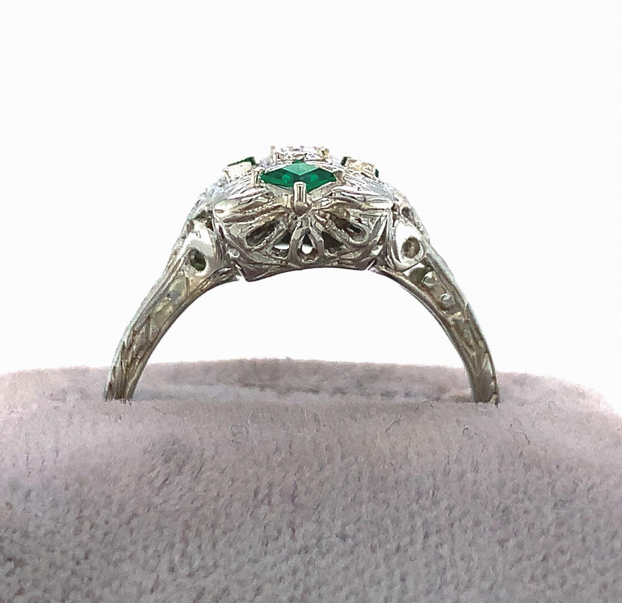  18K white gold filigree diamond ring with synthetic emerald accents. There are 3 round diamonds and 4 specialty cut synthetic emeralds. There are 3 round brilliant cut diamonds measuring about 1.8mm each for a total weigh of about .08cts. The