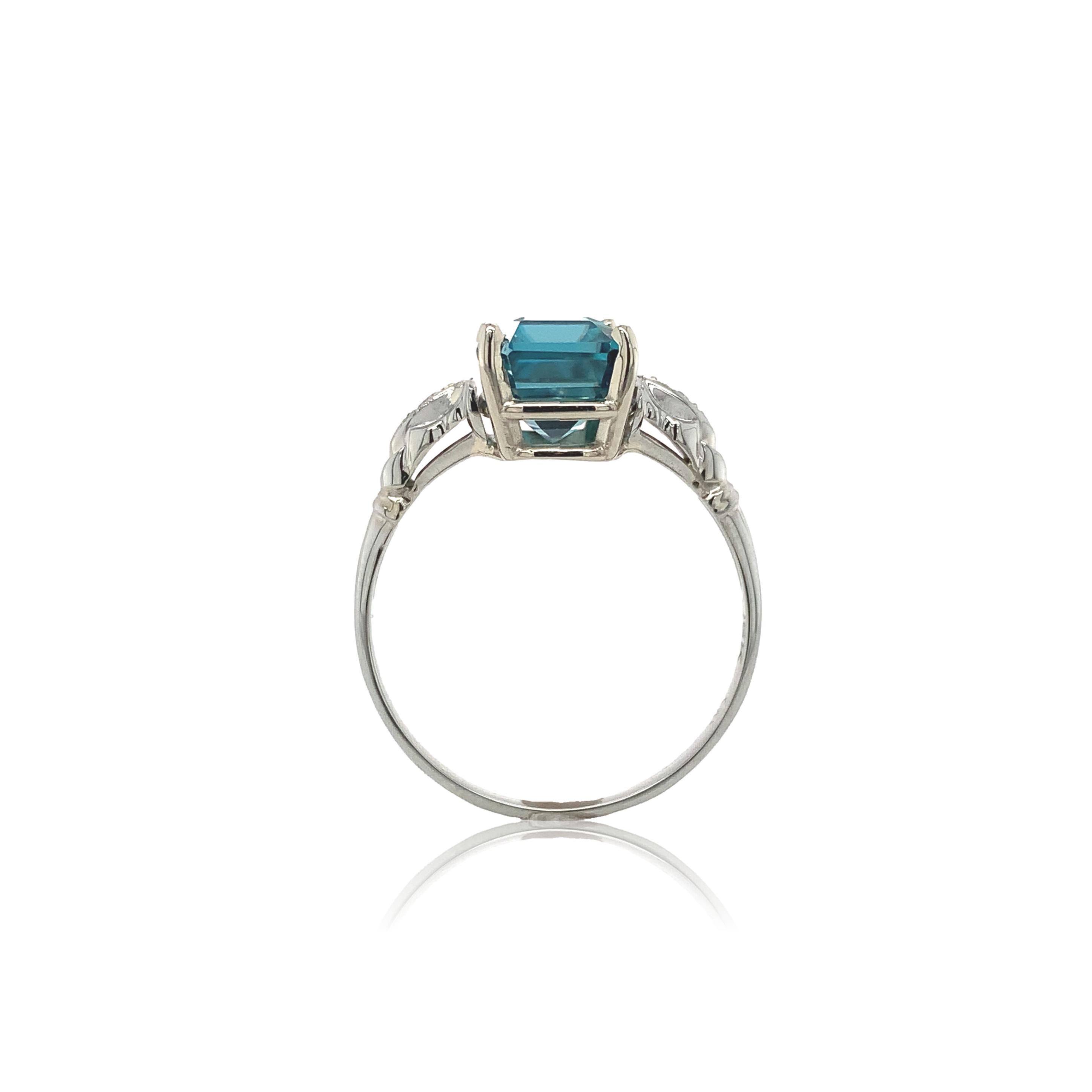 18K white gold 3.99 carat emerald cut teal blue-green zircon and diamond ring. The zircon measures about 8.4mm x 7mm and is accented by 2 round diamonds measuring about 2mm and weighing about .04cts total. Blue zircon is a naturally mined gemstone
