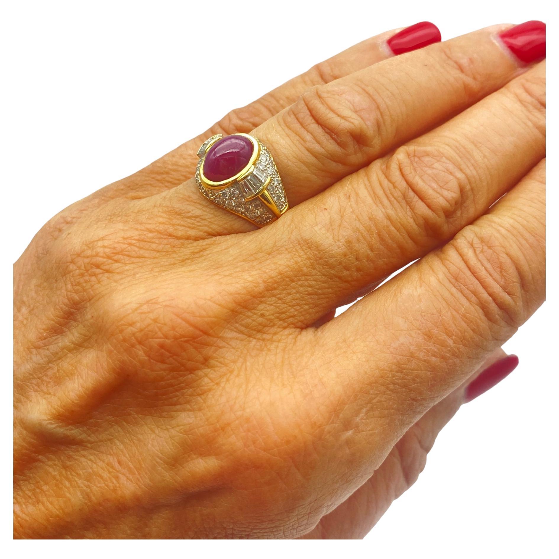 The exquisite dome ring features an oval red ruby shaped in a cabochon and surrounded by diamonds. The ring measures 14.30 mm wide at the top and graduates to a 4.80 mm shank. The ruby is counted as 10 x 8 x 5 mm in diameter and estimated as a 4.50