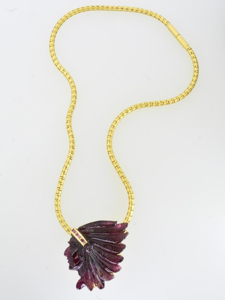 The carved deep red tourmaline (rubelite) of a proud and noble figure with the dress of a native American Indian chief respected by his people.

It is 18K and marked on the verso. This well carved stone depicts a three dimensional figure with very