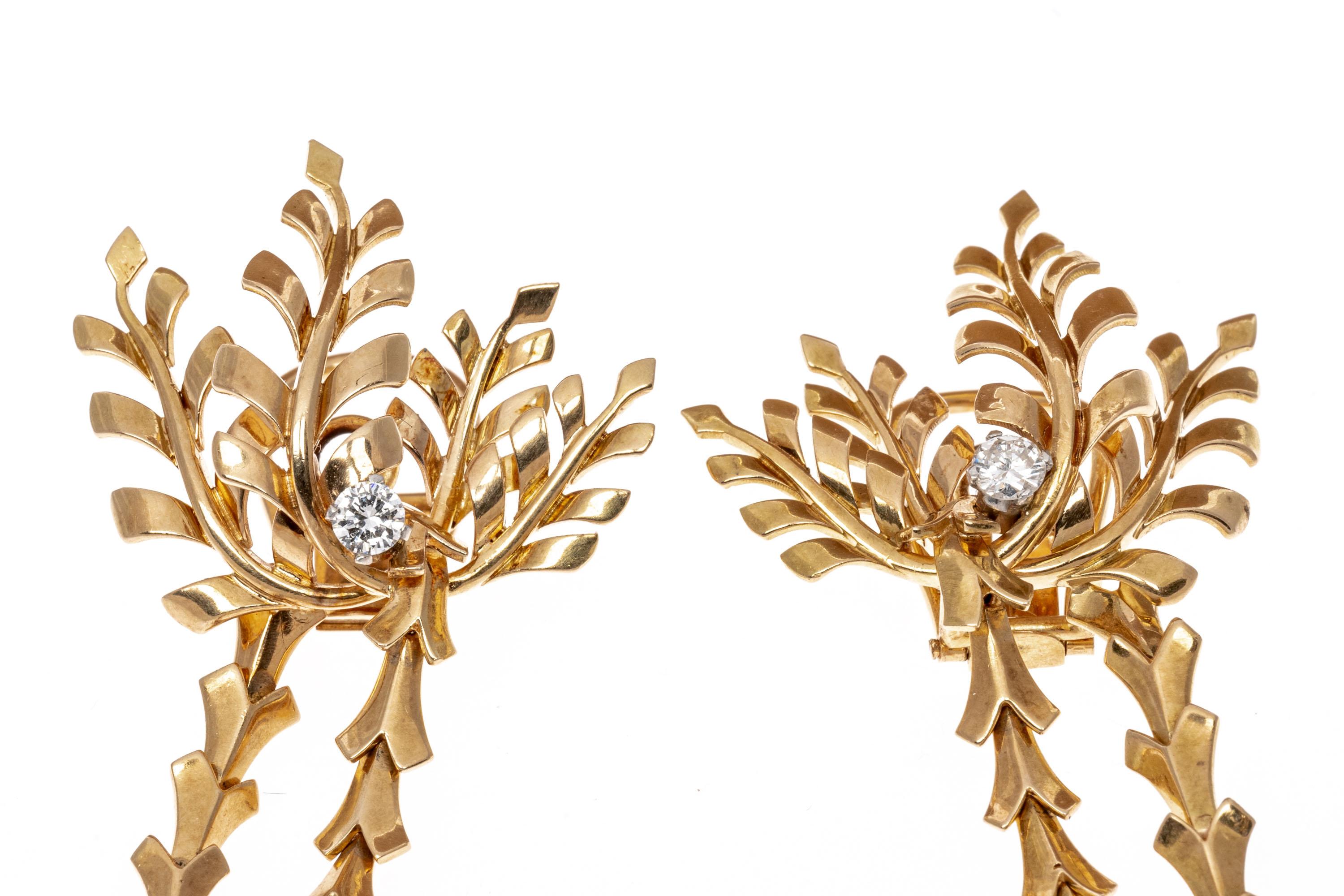 These 18K yellow gold impressive, sophisticated and beautifully made earrings are a leaf motif. The tops are set with four curved leaves, with a round brilliant cut diamond, prong set, set at the base. Suspended from the top are two vertical,