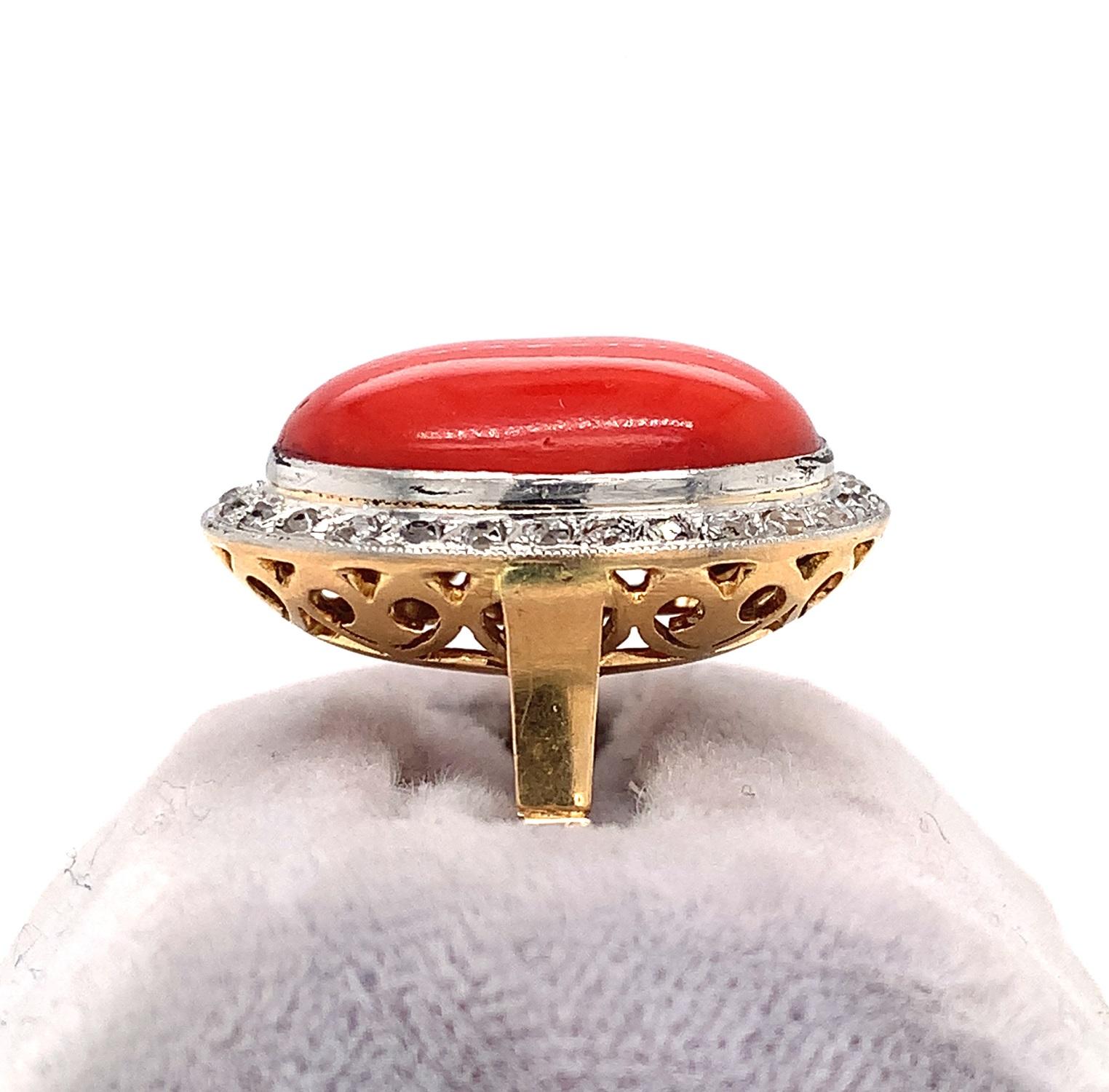18K yellow gold with platinum top ring featuring a cabochon ox blood coral accented with a border of small polki/rough cut diamonds. The oval coral cabochon measures about 18.5mm x 12.5mm x 6mm and has a dark orangey-red color with a nice polish. 