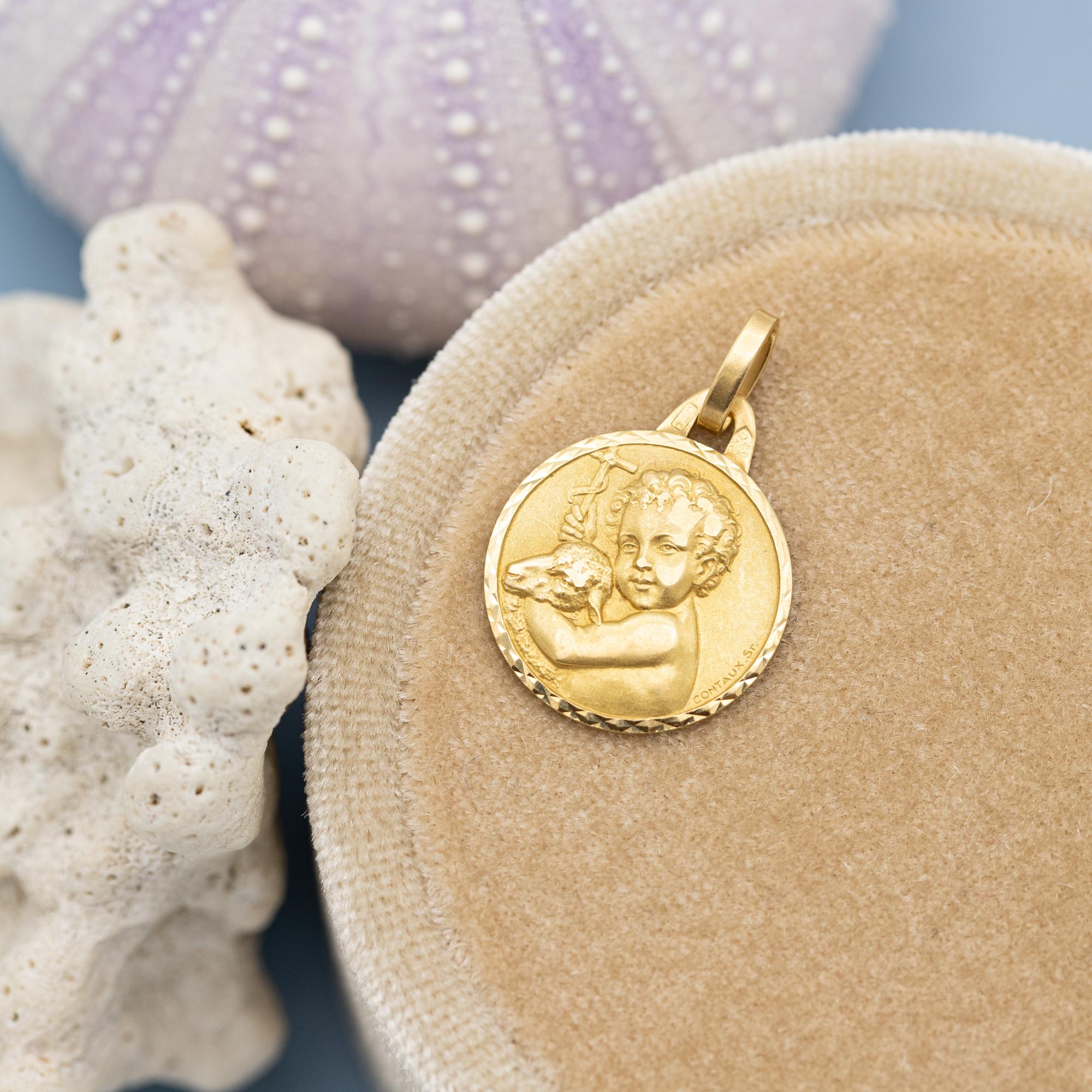 For sale is this 18 Karat yellow gold baby pendant. This beautiful detailed medal depicts a little child with curly hear, holding a cross and cuddling with a Lamb. In Christian art and iconography, an angel with a lamb and a cross often symbolizes