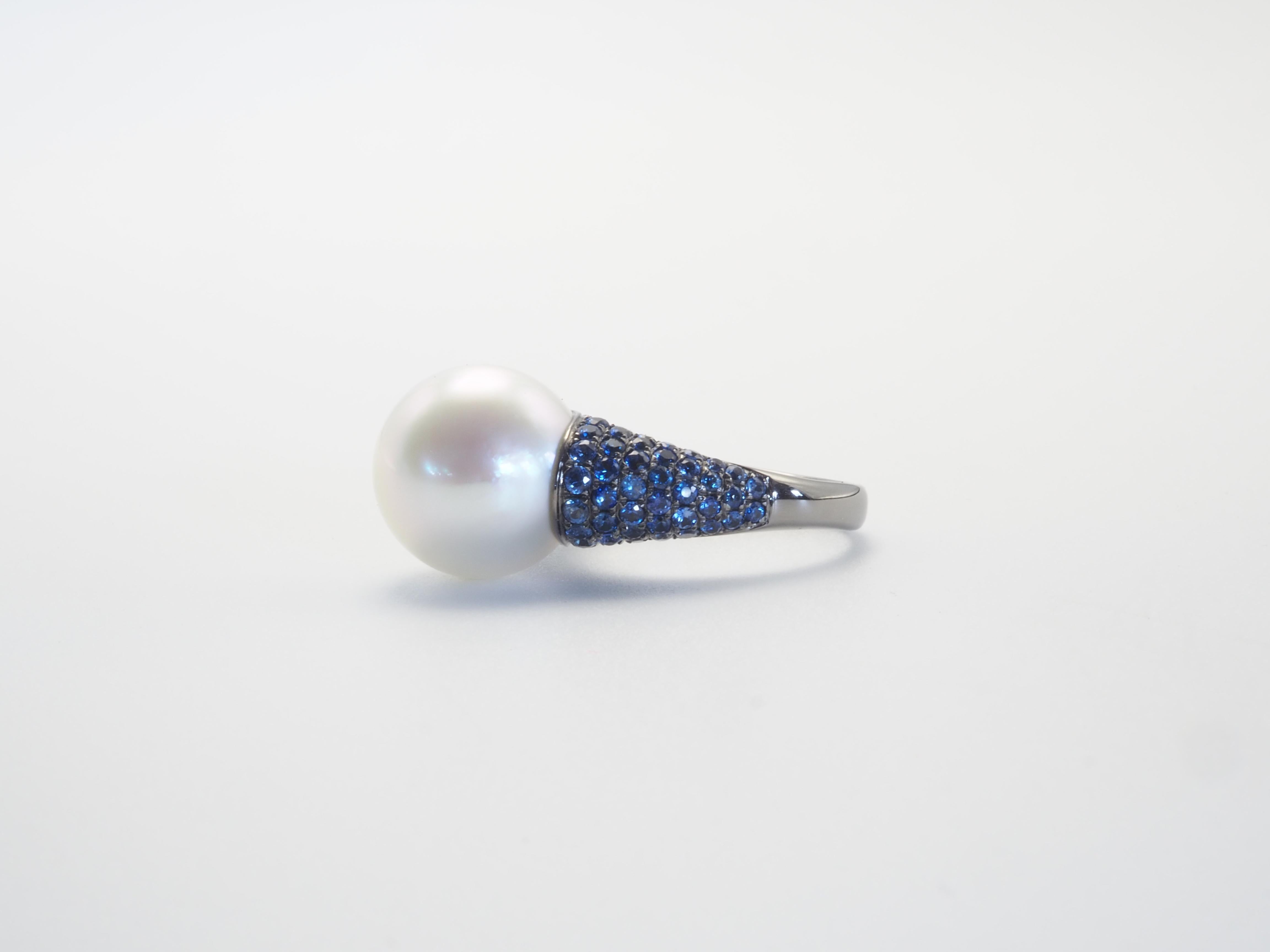 This brilliant ring is adorned with 1 rare and beautiful White south sea pearl! The pearl is perfectly round and has little to no visible blemishes. The diameter of the pearl is over 13 mm. The accenting clusters of blue sapphires are bright and of