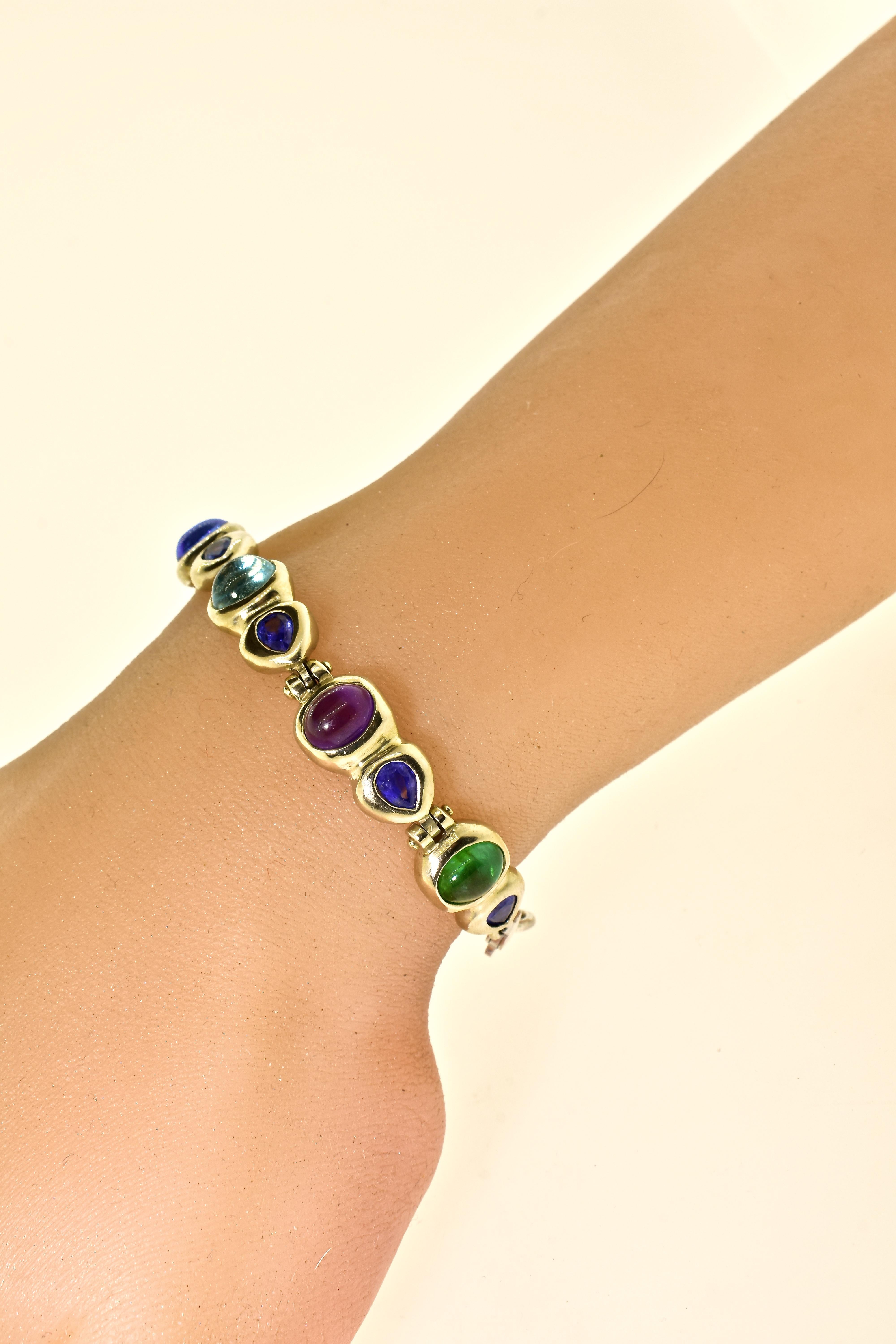 18K bracelet of contemporary design featuring 6 fine colored stones.  There are 2 fine emeralds, (4.1 cts.), 7 sapphires (2.9 cts.) a Rhodolite garnet (2.1 cts.) 2 Aquamarines (3.9 cts), and an amethyst (1.8 ct). All weights are estimated by our