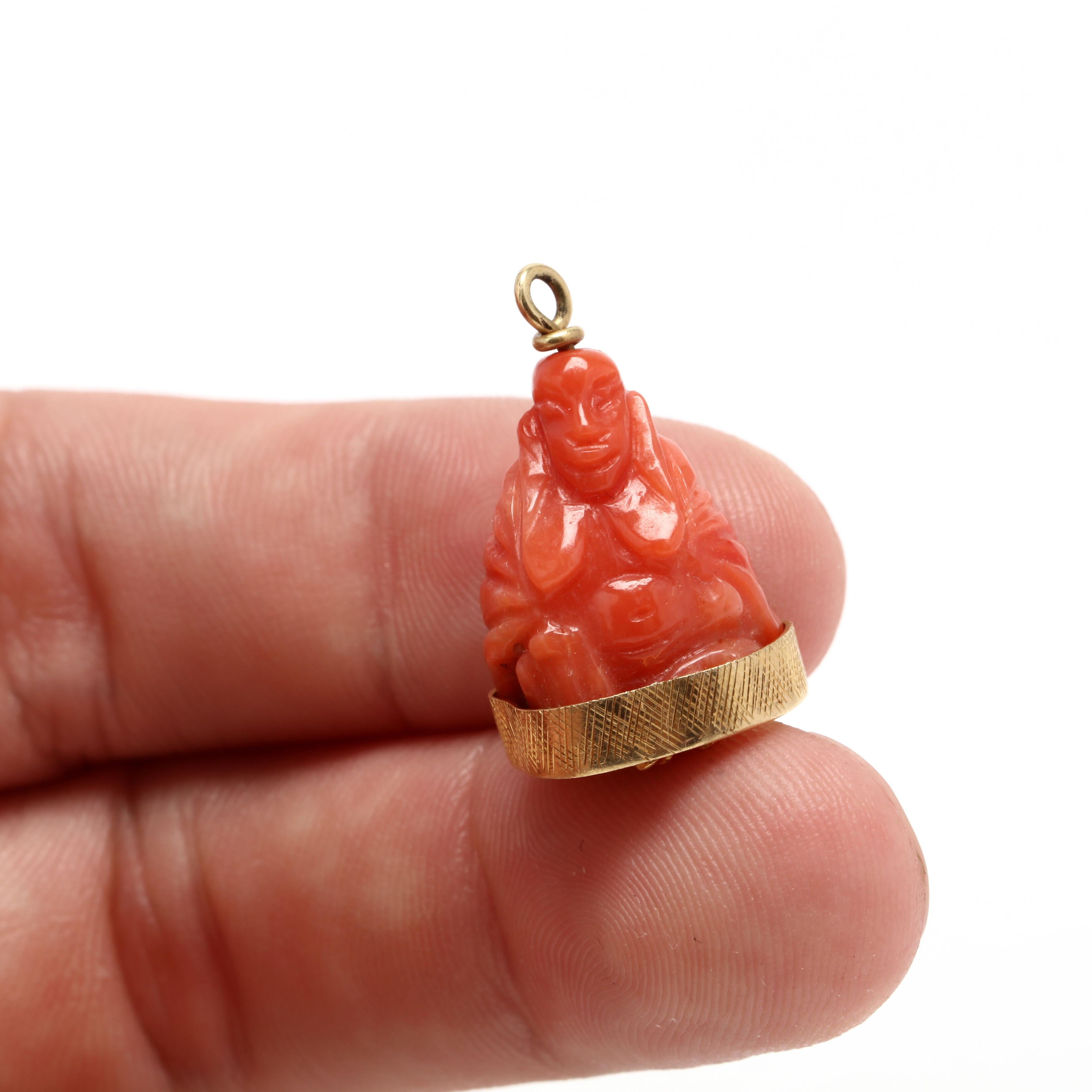 A vintage 18 karat yellow gold carved coral buddha charm. This charm features a carved coral stone depicting a buddha with a textured gold bezel and an applied rope floral motif on the bottom.



Length: 15/16 in.



Width: 5/8 in.



Weight: 3.3