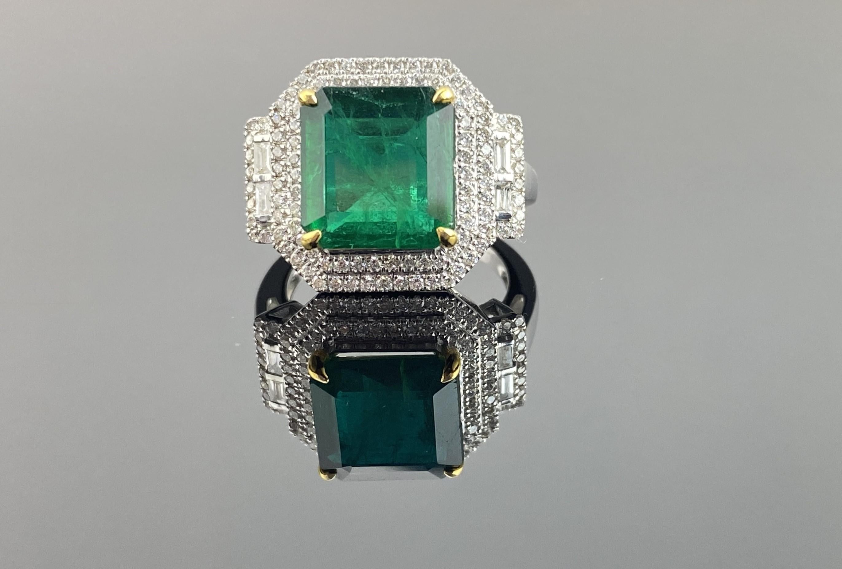 The centerpiece is a vibrant 4.86-carat emerald originating from Zambia, measuring 11 x 10.5 mm, set in 18K white gold and surrounded by a double halo of round and baguette diamonds, totaling 0.74 carats. The ring is made in 18K white gold which